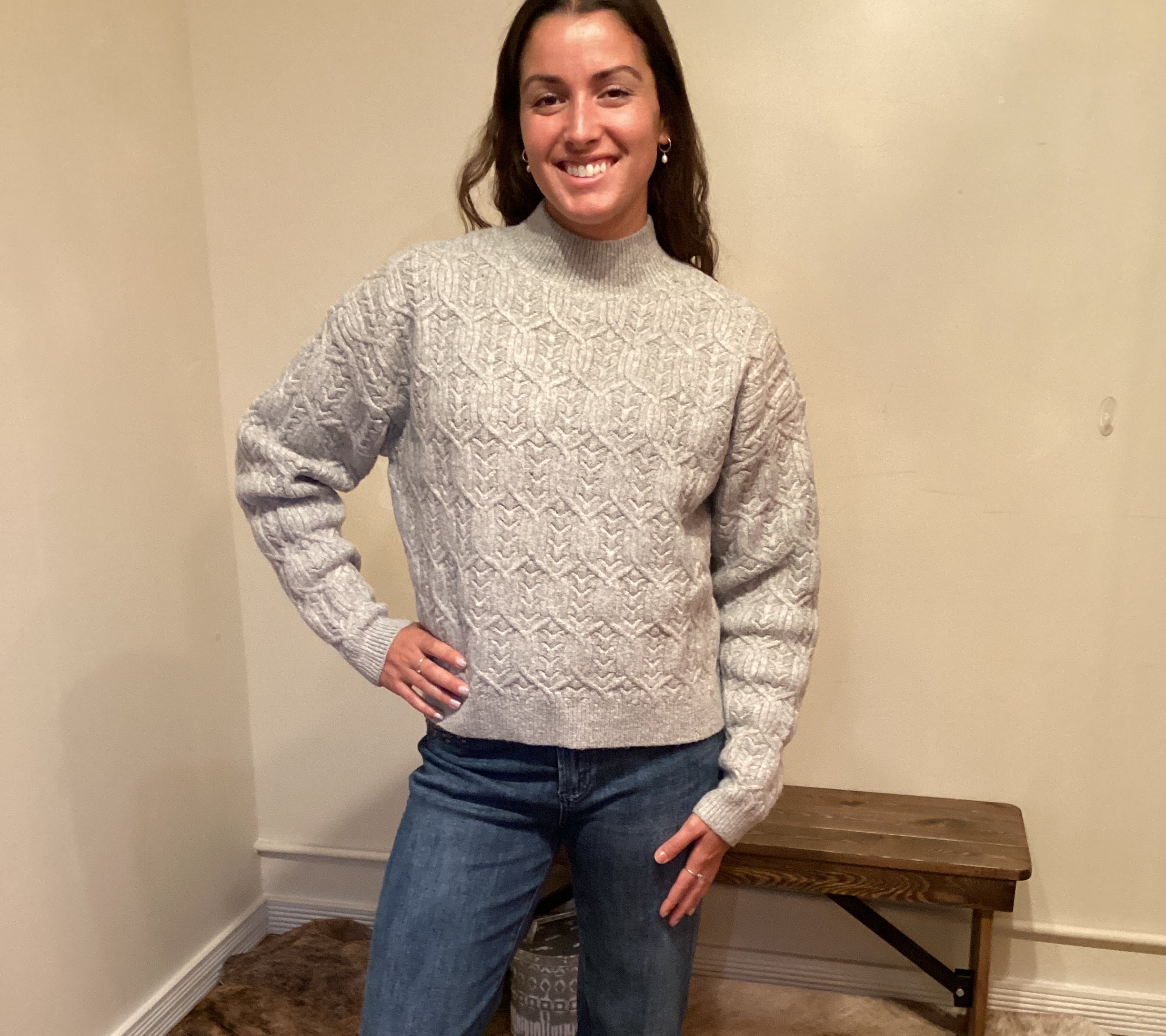 Person wearing a gray sweater and blue jeans standing on a carpeted floor.
