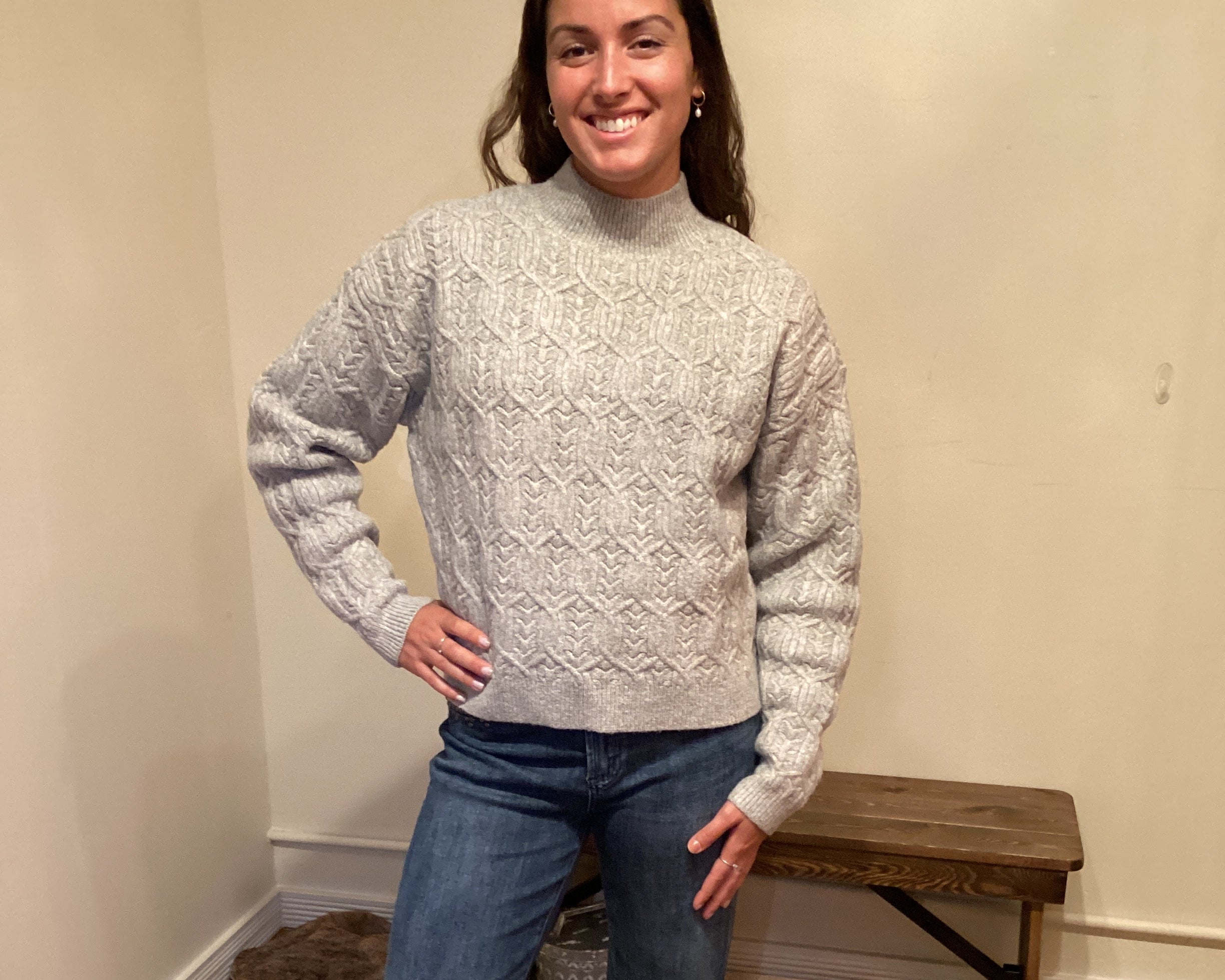 Person wearing a gray sweater and blue jeans standing on a carpeted floor.