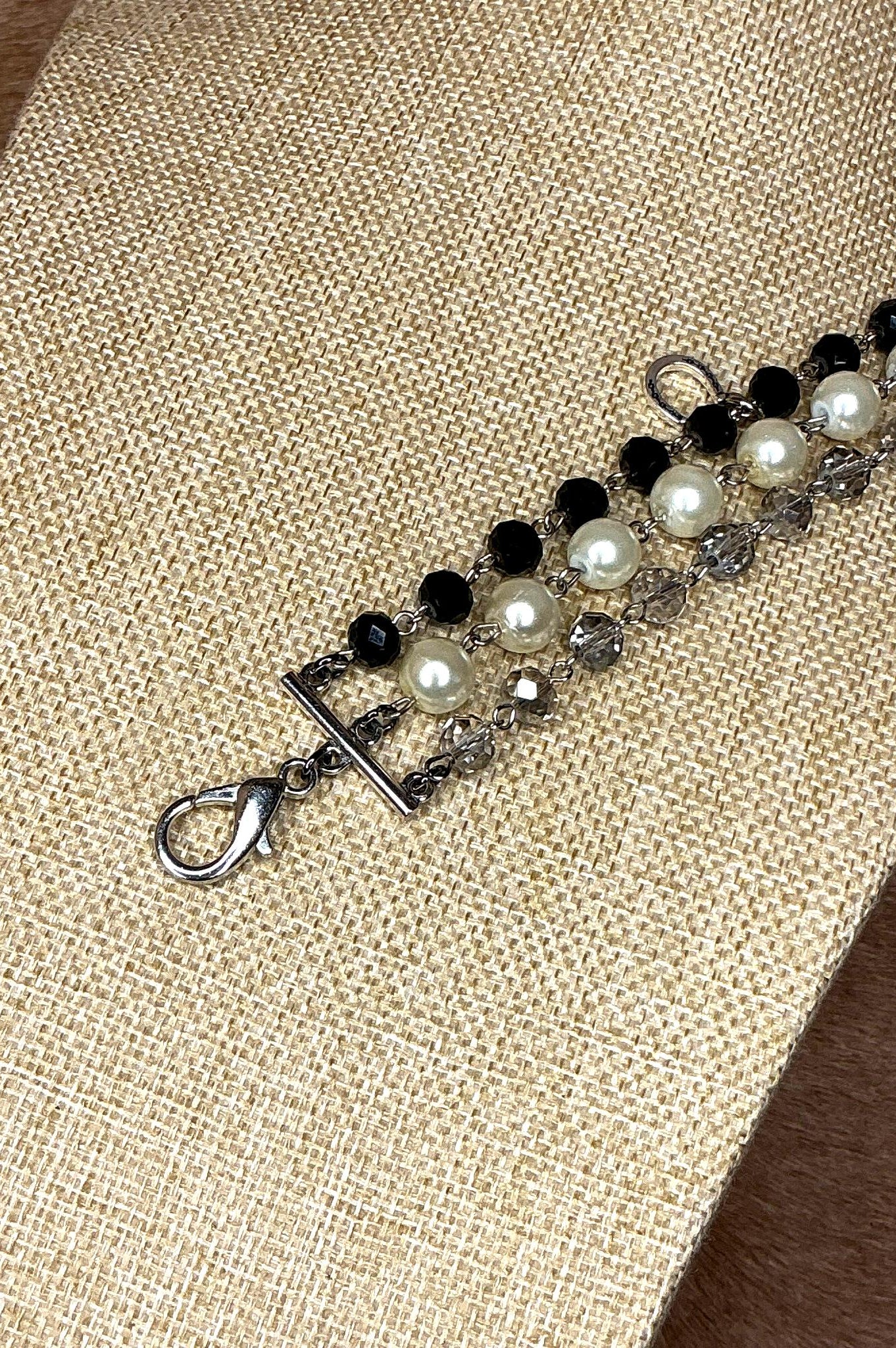 Silver lobster clasp detail of handcrafted bracelet with pearls, black beads, and crystals on silver chain.