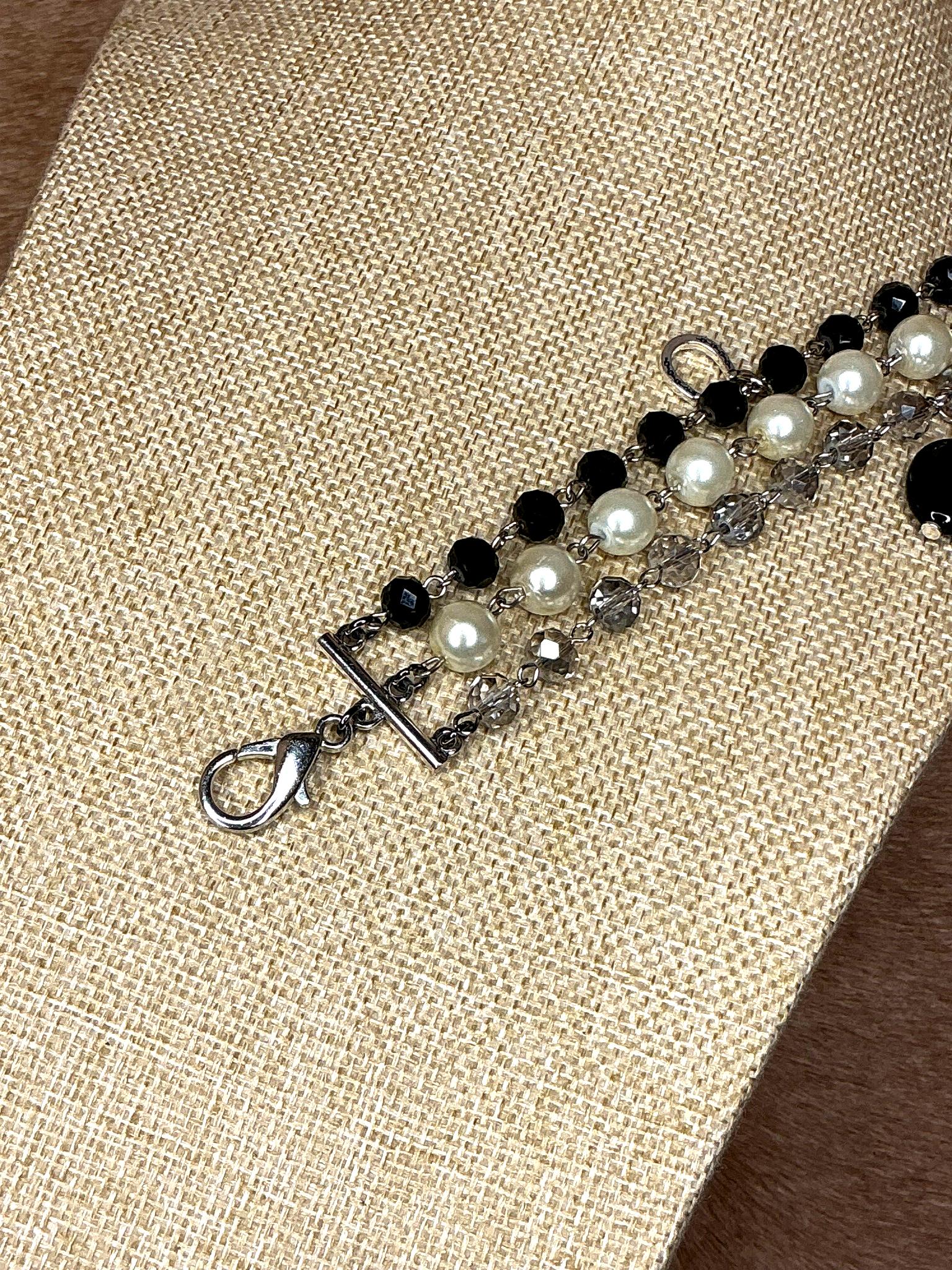 Silver lobster clasp detail of handcrafted bracelet with pearls, black beads, and crystals on silver chain.