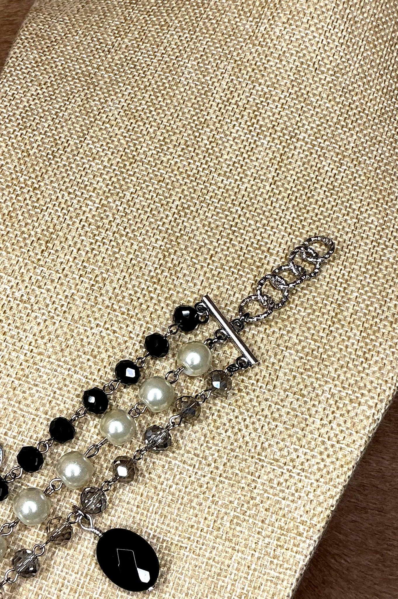 Silver chain clasp detail of triple-strand bracelet with alternating black and white pearls and crystals