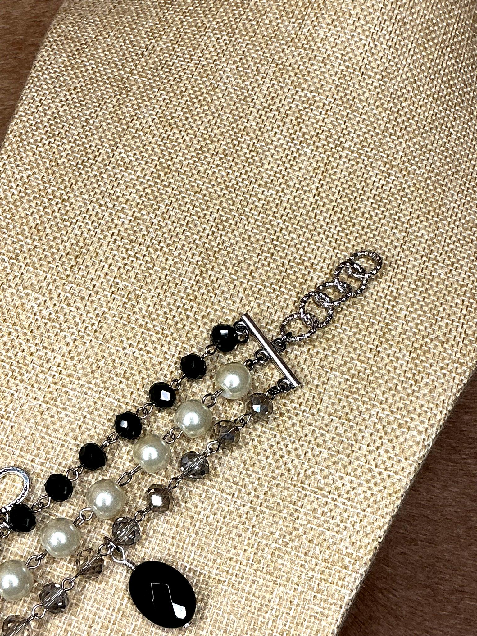 Silver chain clasp detail of triple-strand bracelet with alternating black and white pearls and crystals