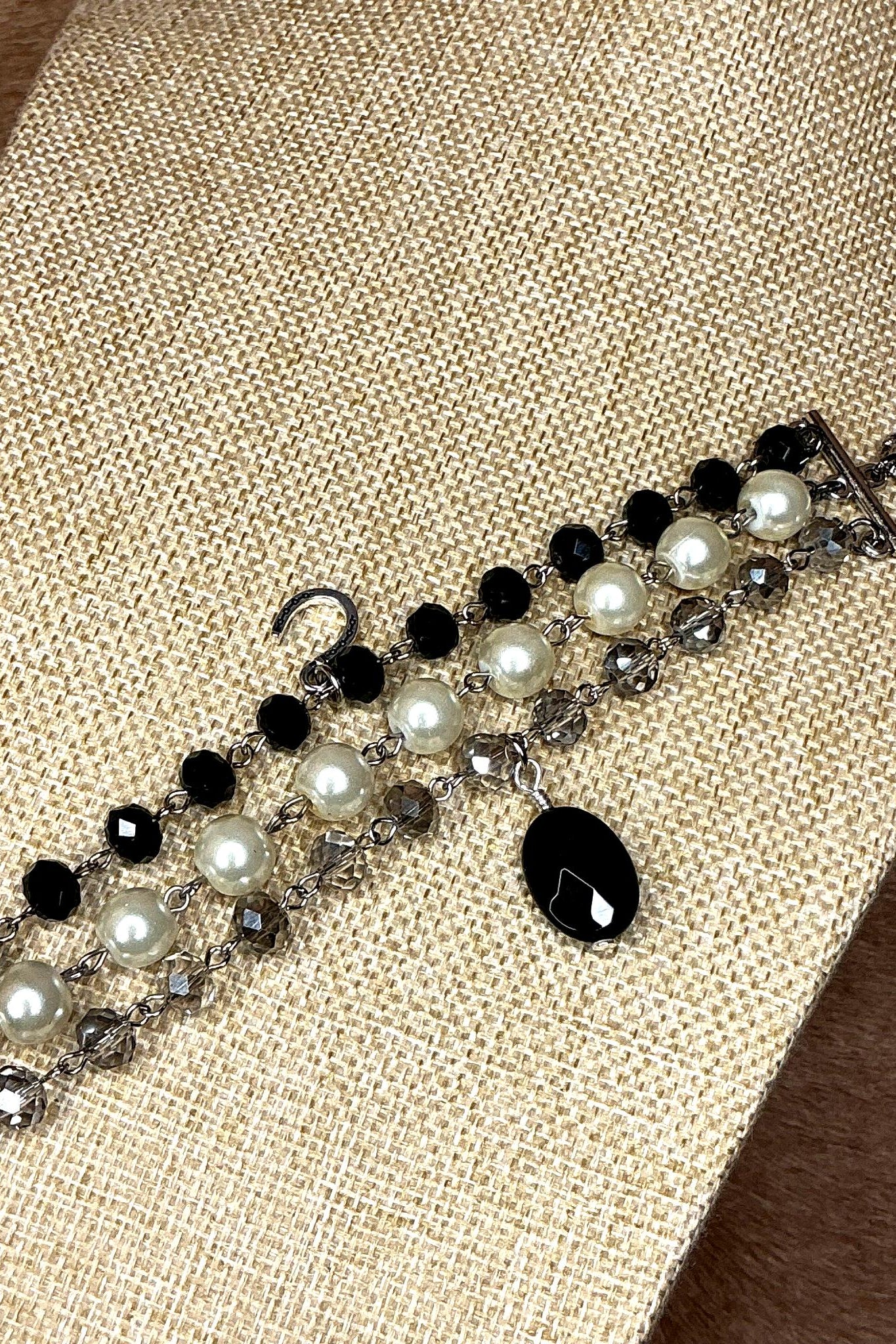 Detailed view of beaded bracelet featuring black and white pearls with silver chain links and dangling black teardrop charm
