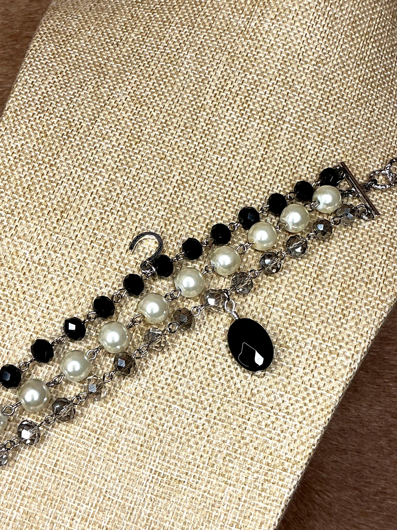 Detailed view of beaded bracelet featuring black and white pearls with silver chain links and dangling black teardrop charm