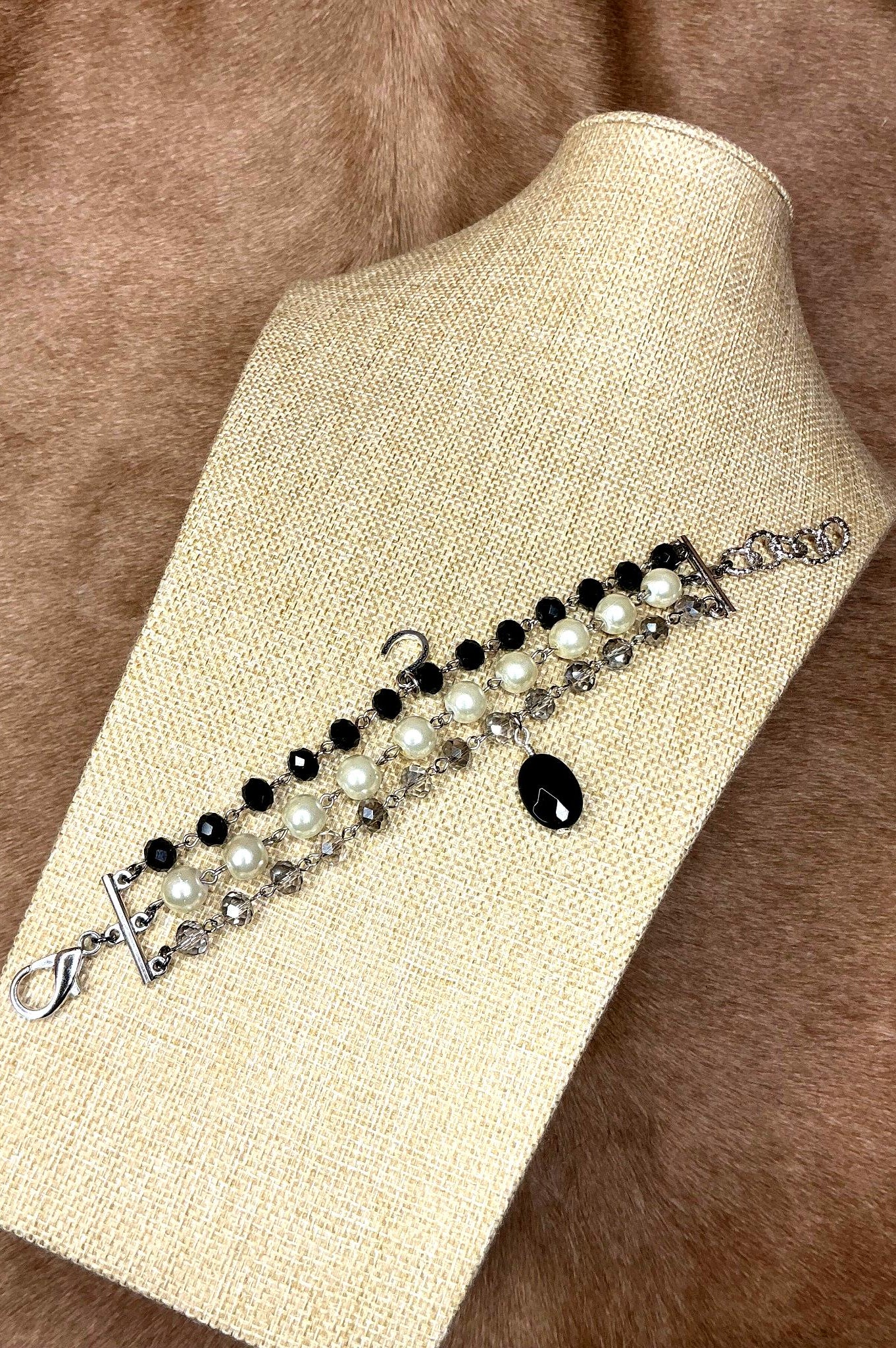 Handcrafted triple-strand bracelet with black beads, white pearls, and faceted crystals on silver chain with black teardrop charm
