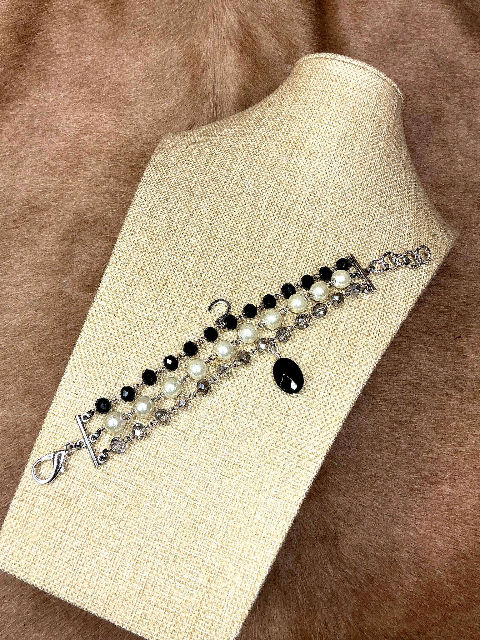 Handcrafted triple-strand bracelet with black beads, white pearls, and faceted crystals on silver chain with black teardrop charm