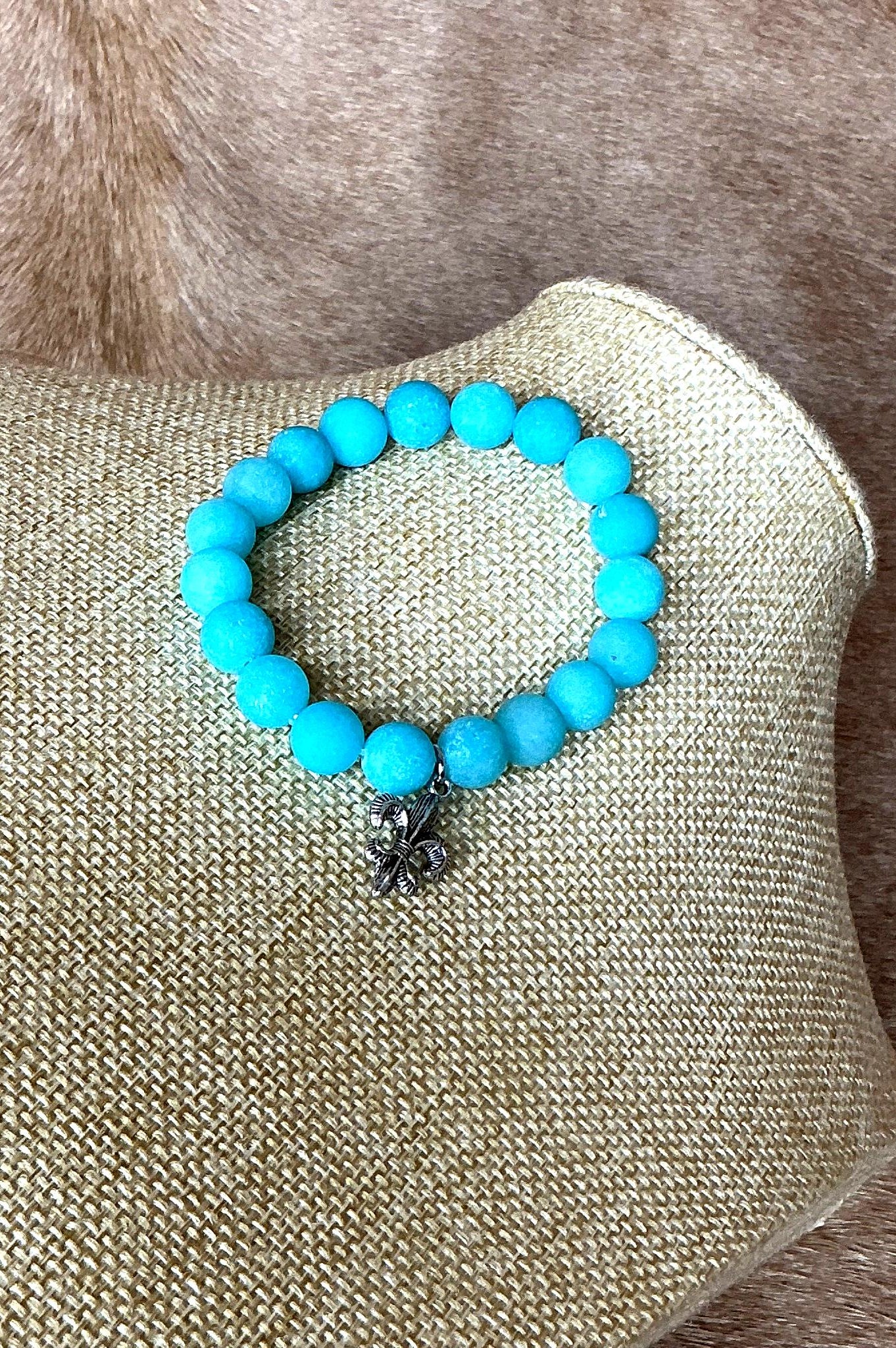 Close-up view of turquoise bead bracelet featuring a detailed silver fleur-de-lis charm