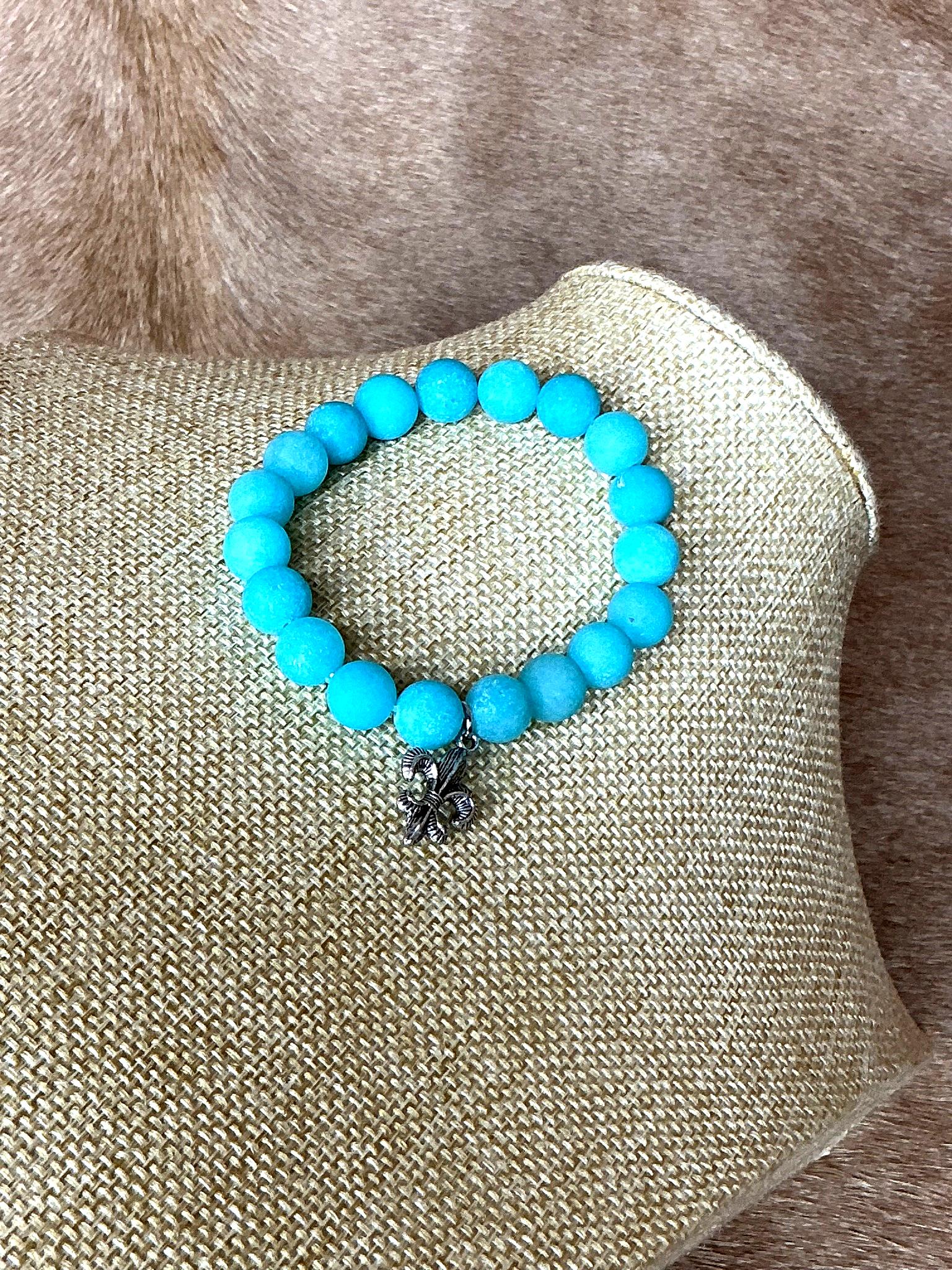 Close-up view of turquoise bead bracelet featuring a detailed silver fleur-de-lis charm