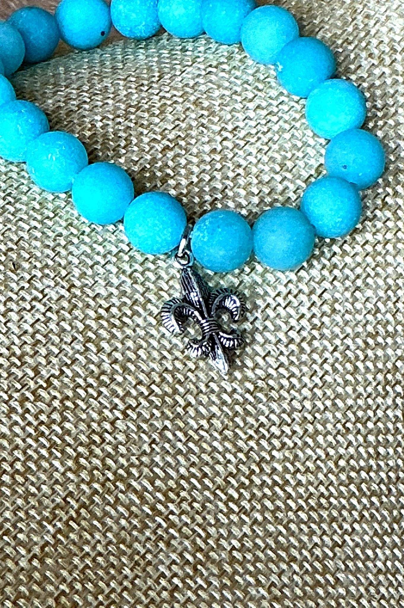 Close-up view of turquoise bead bracelet featuring a detailed silver fleur-de-lis charm