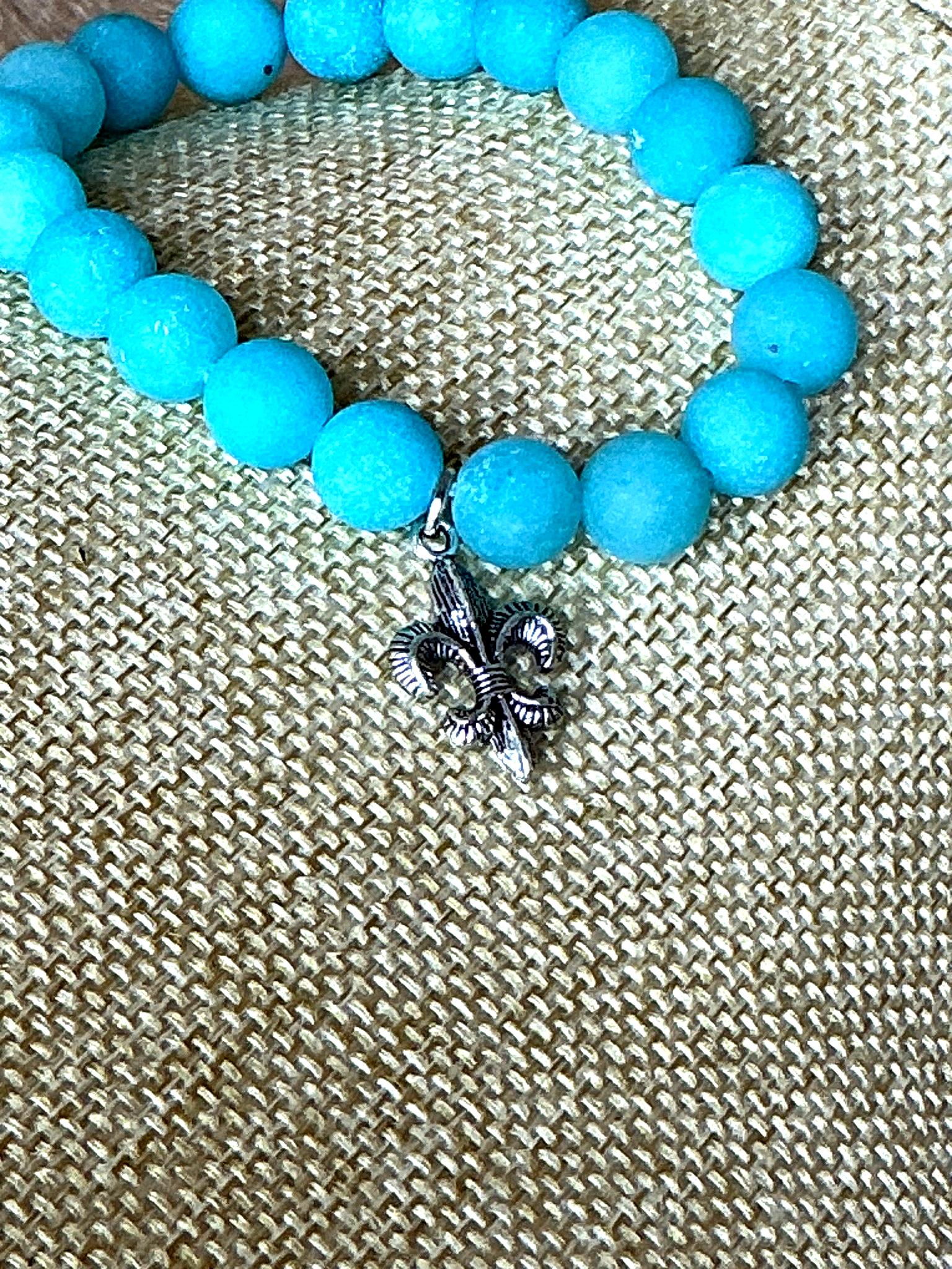 Close-up view of turquoise bead bracelet featuring a detailed silver fleur-de-lis charm
