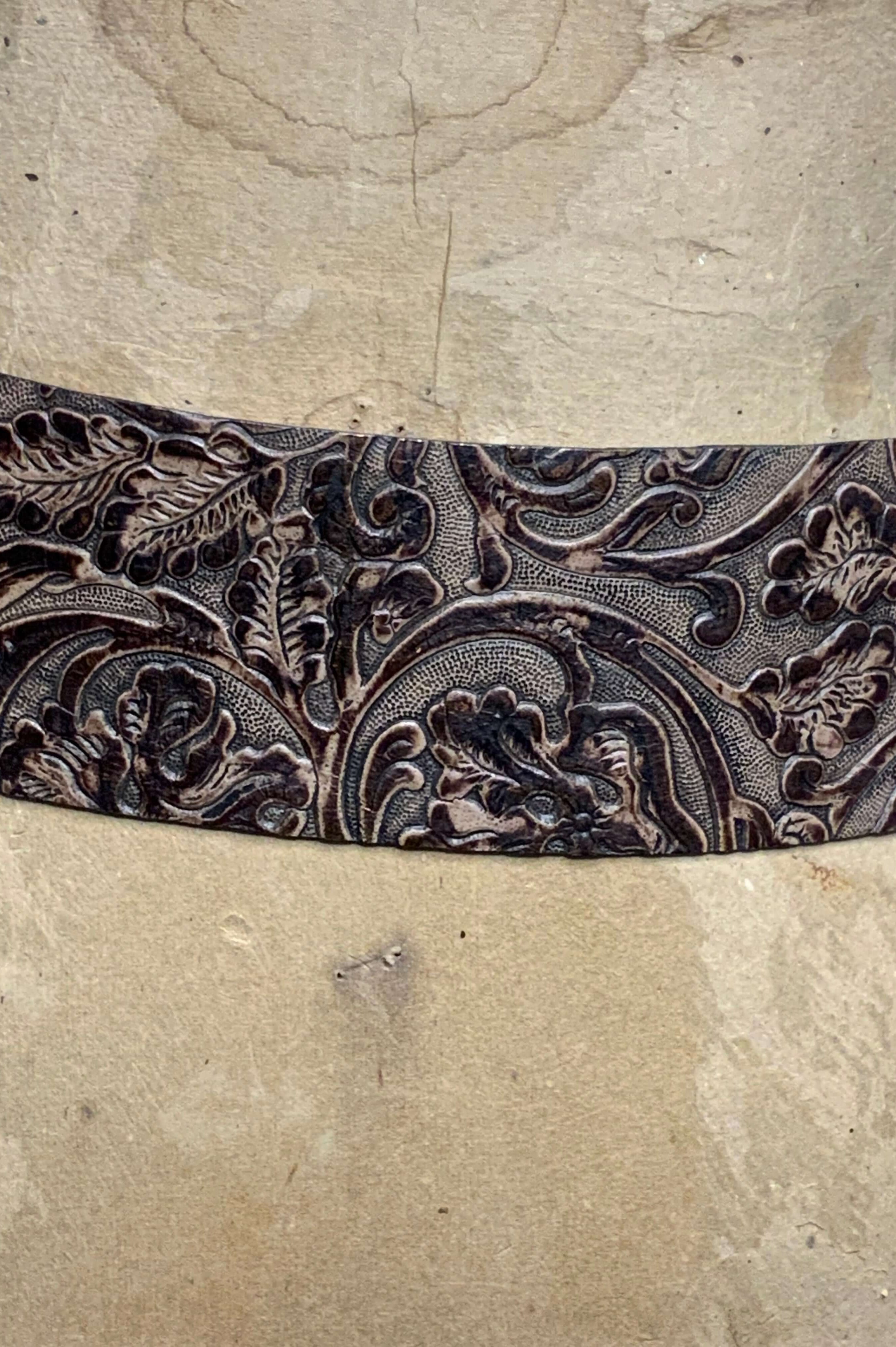Decorative leather belt with intricate floral patterns on a textured beige background