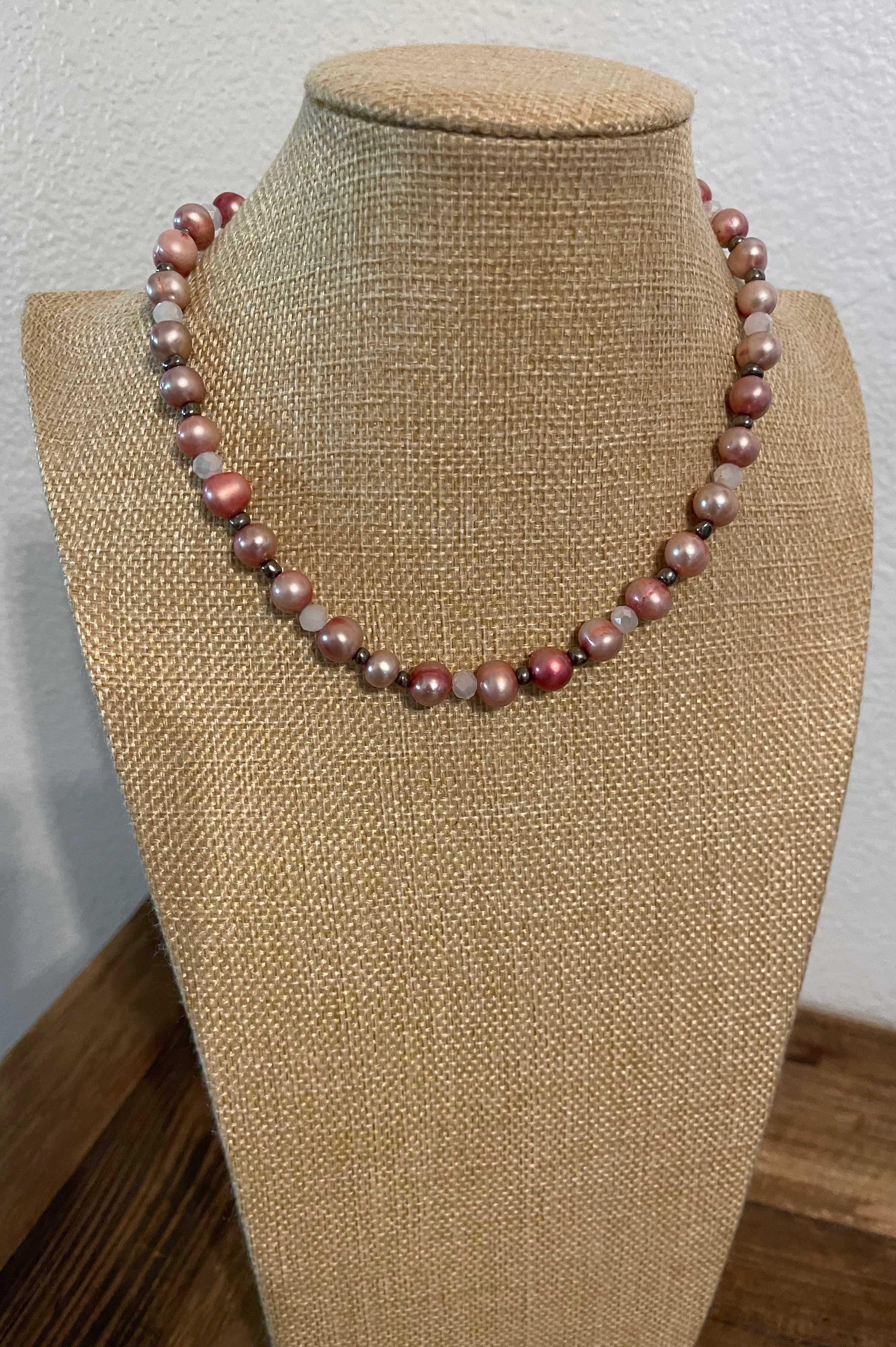 Necklace with pink dyed pearls and white crystals with silver bead accents on a beige mannequin.