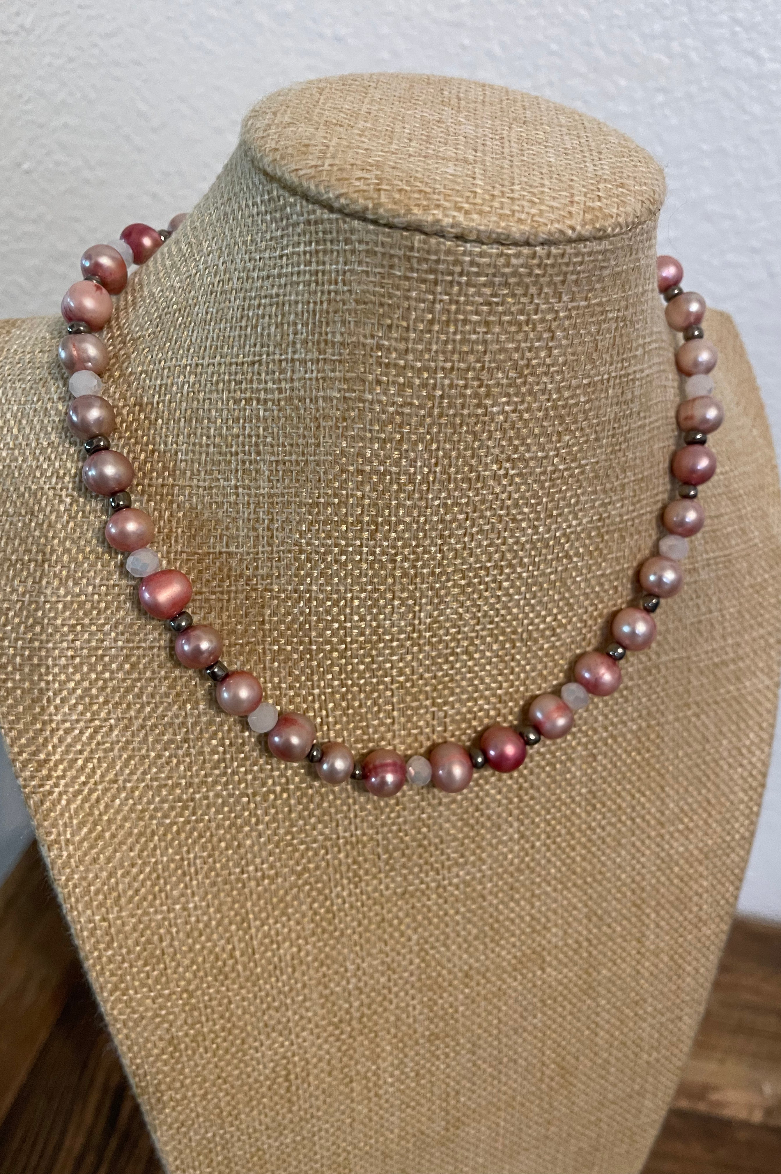 Necklace with pink dyed pearls and white crystals with silver bead accents on a beige mannequin.