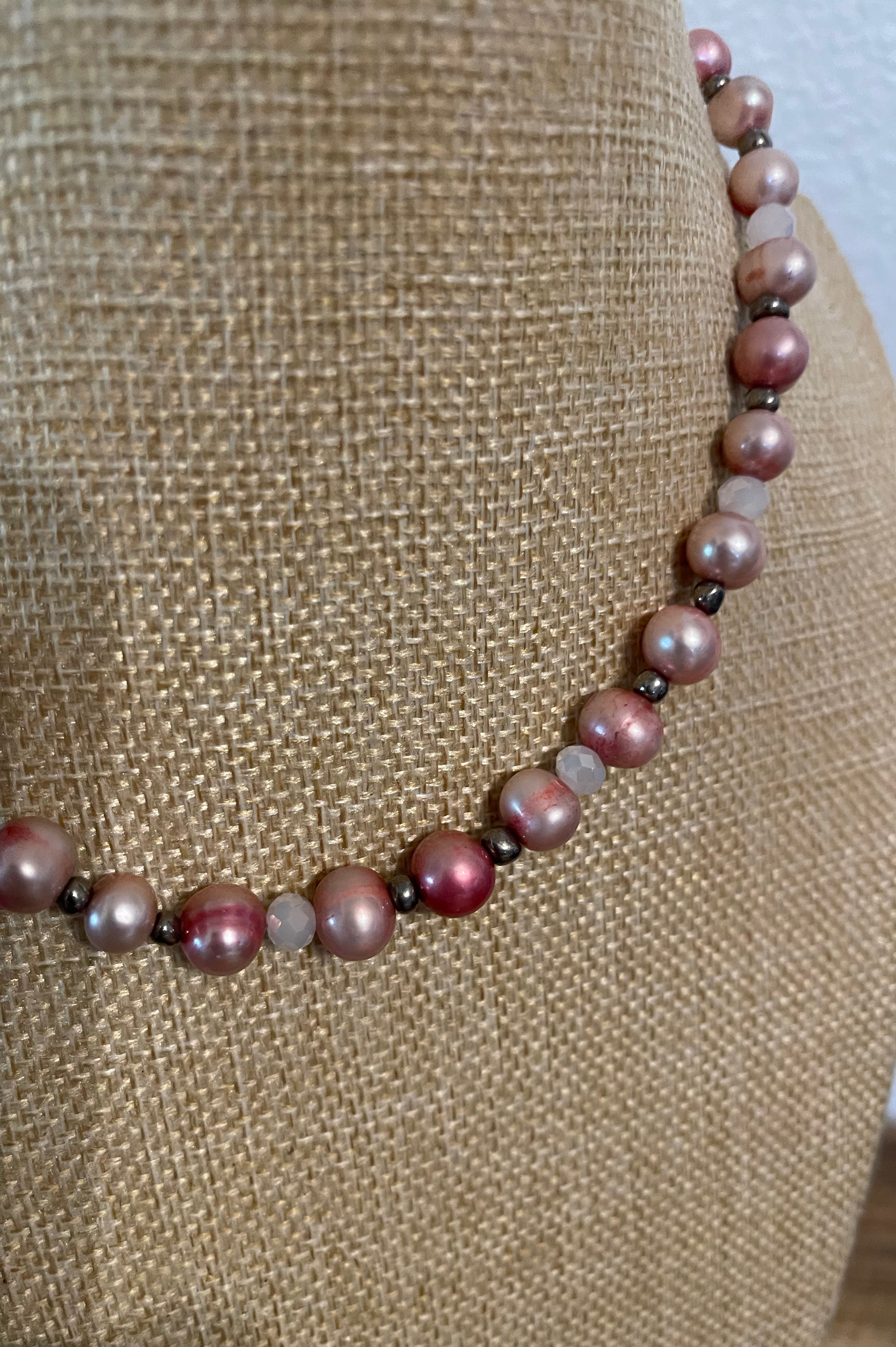 Necklace with pink dyed pearls and white crystals with silver bead accents on a beige mannequin.
