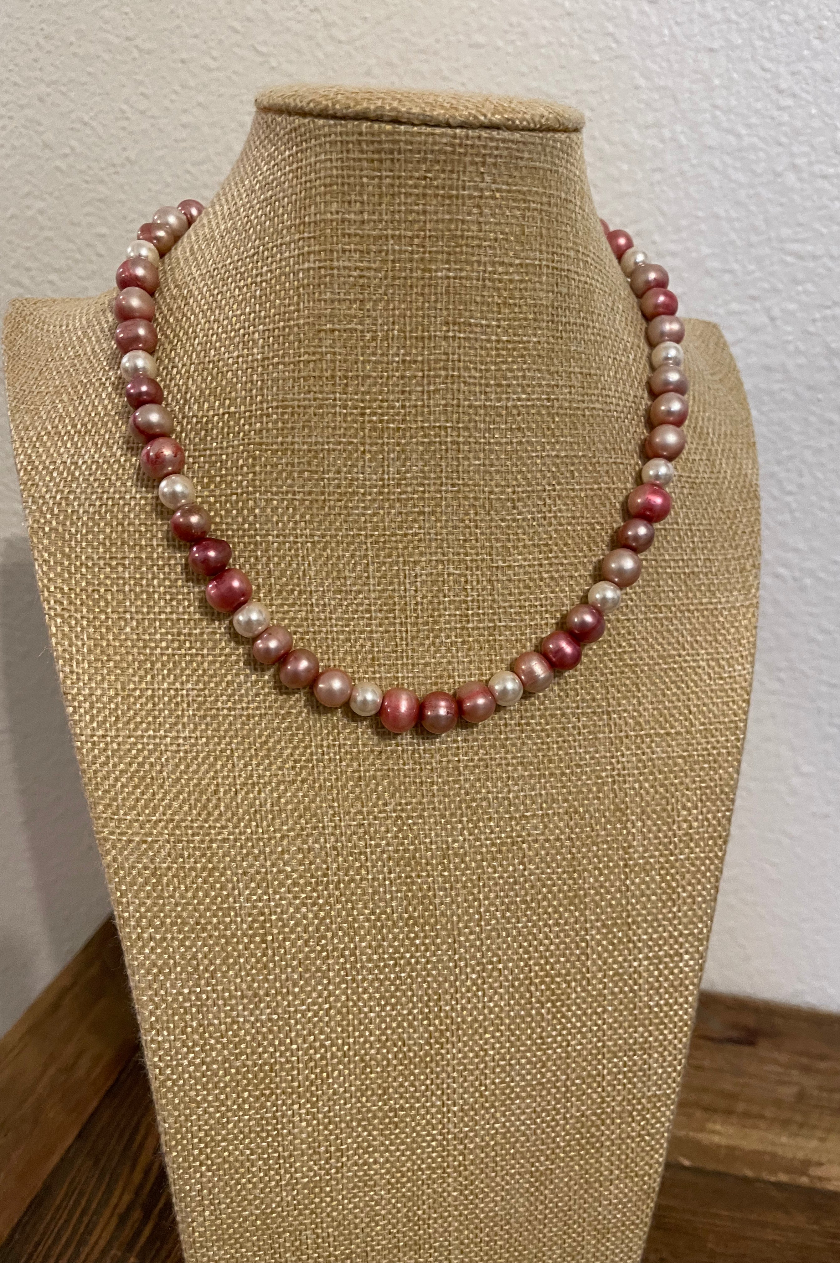 Pink and ivory pearl necklace on a beige mannequin bust against a white wall.