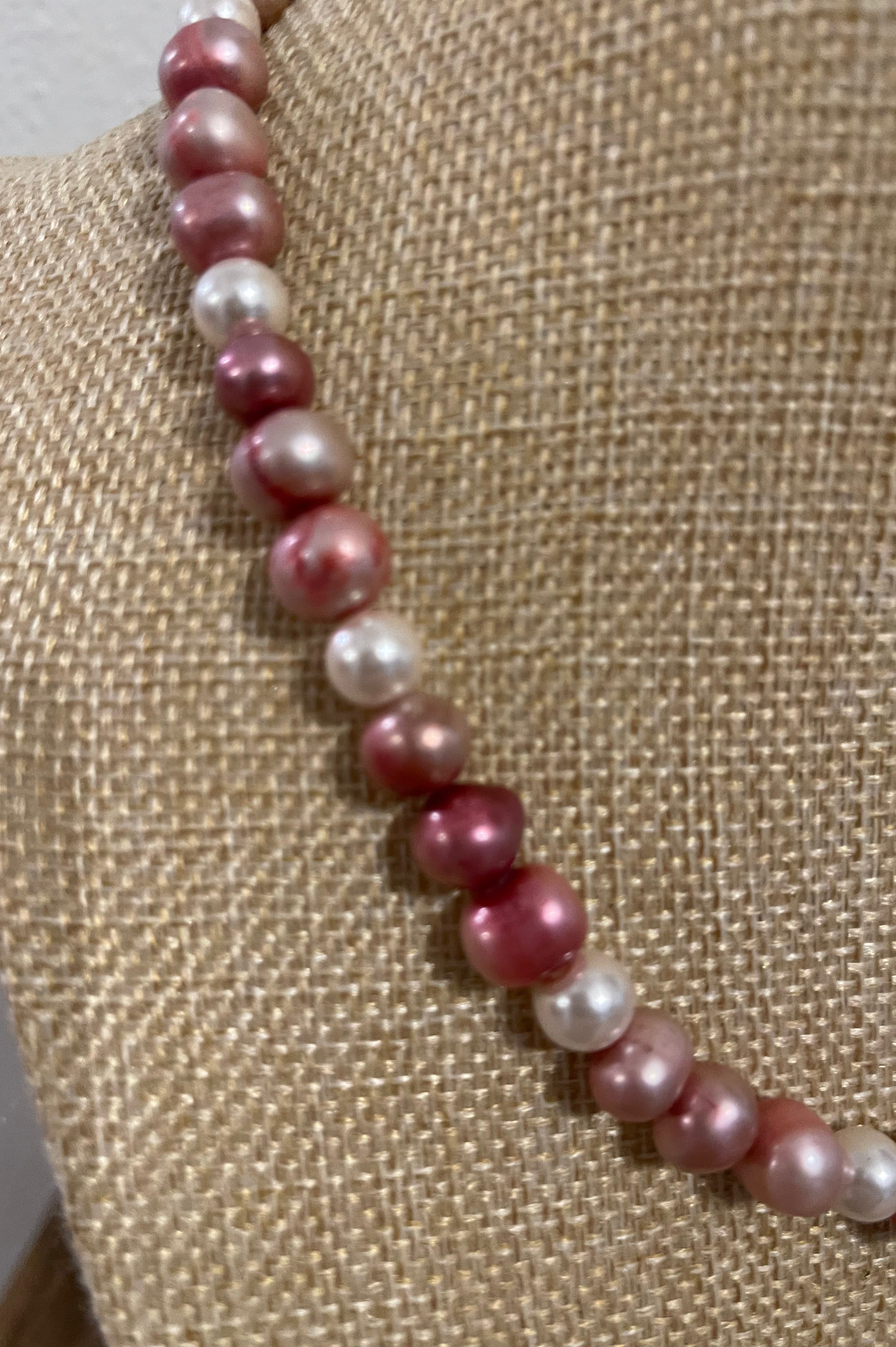 Necklace with pink and white pearls on a textured beige surface