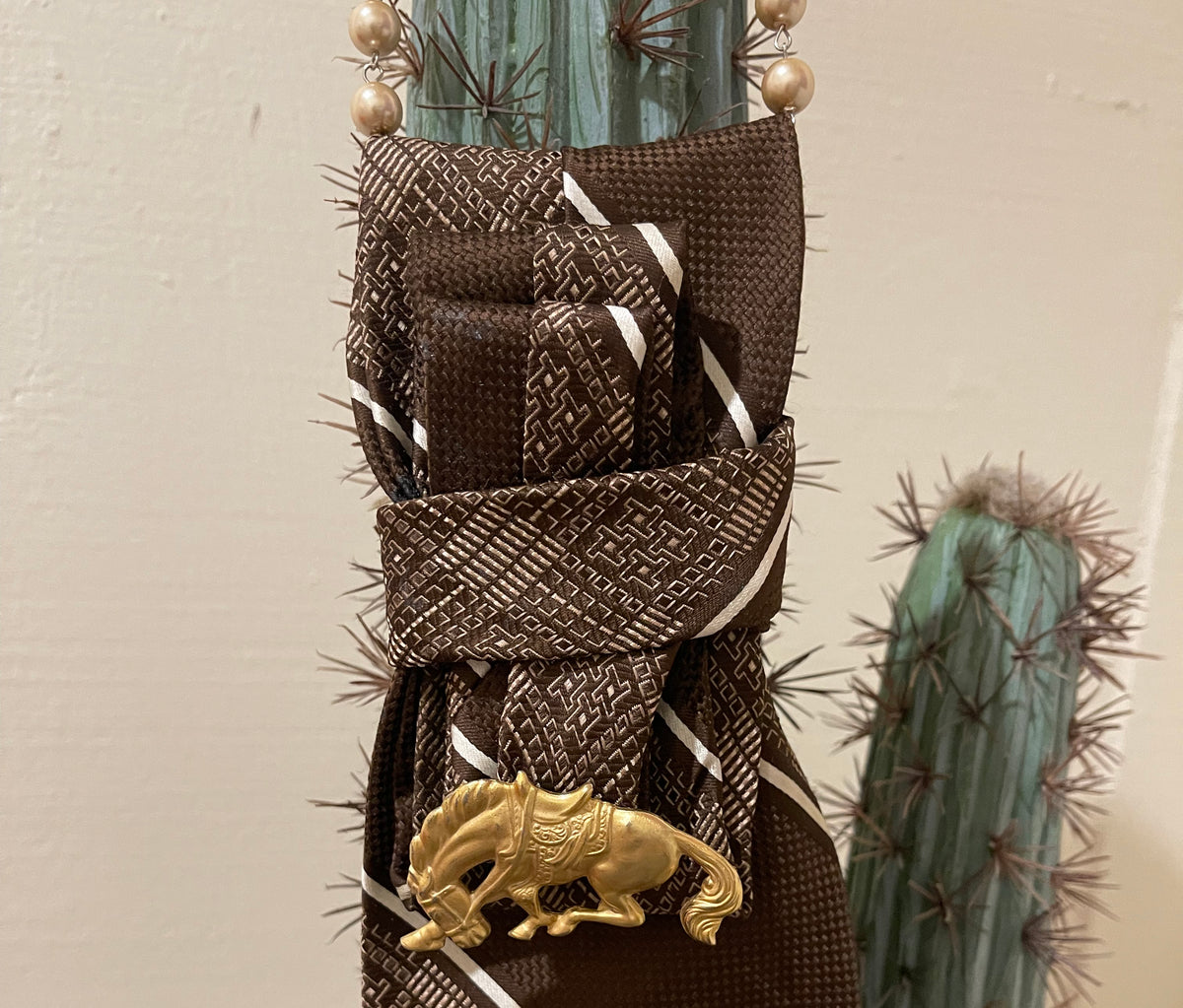 Handcrafted vintage tie necklace by Copper & Lace Western Boutique featuring an authentic 1970s brown patterned necktie, champagne pearl strand, and vintage gold-tone horse brooch.