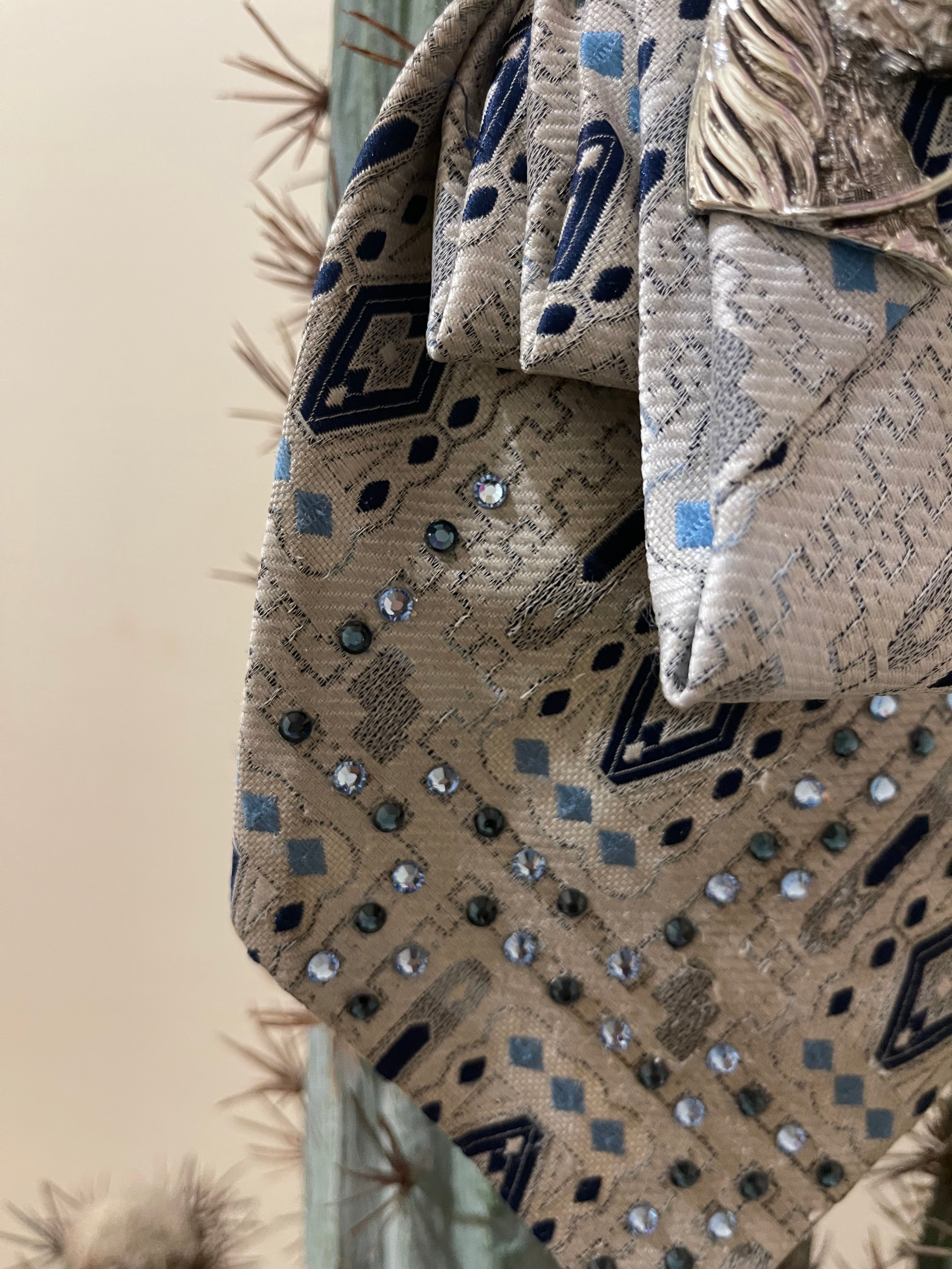 Handcrafted vintage tie necklace by Copper & Lace Western Boutique featuring an authentic 1970s silver, navy, and blue patterned necktie with rhinestone embellishments, vintage silver horse head brooch, and ornate silver chain.