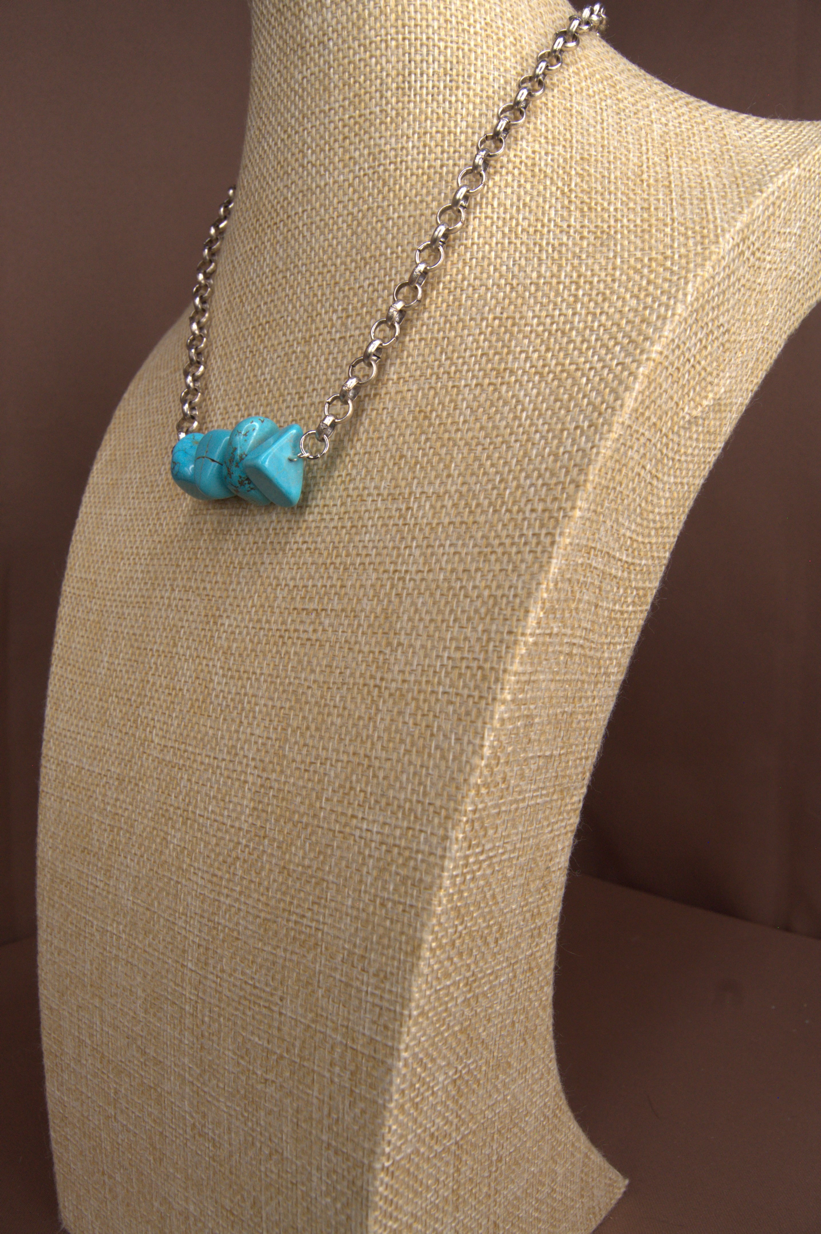 Turquoise stone necklace on a mannequin bust with a brown background