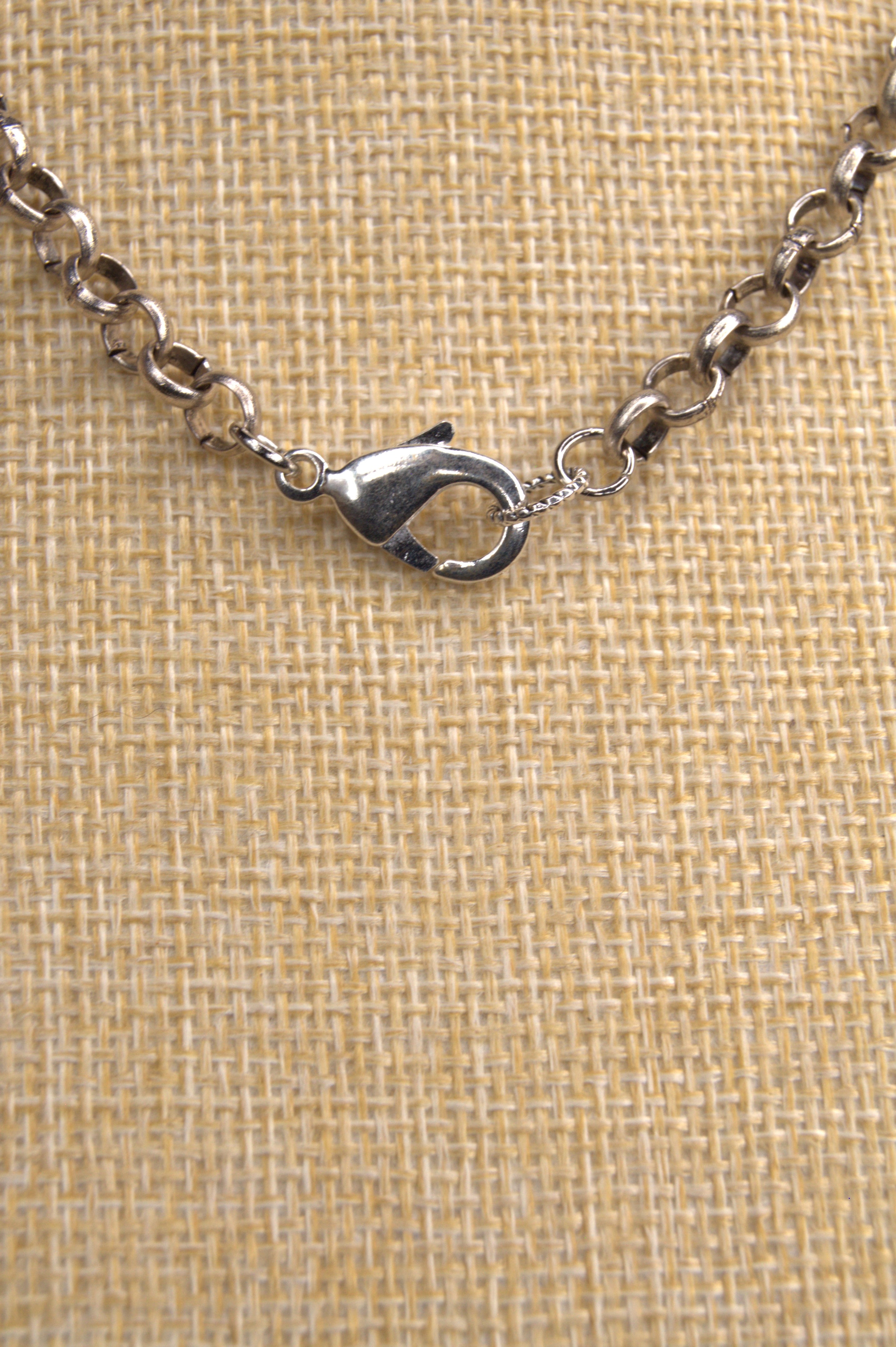 Close-up of a silver necklace with lobster. claw clasp on a textured beige background