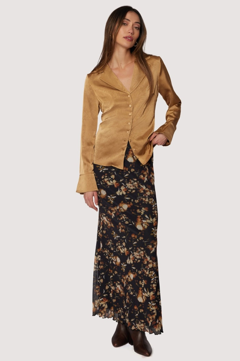 Woman wearing a gold jacket and floral skirt on a white background