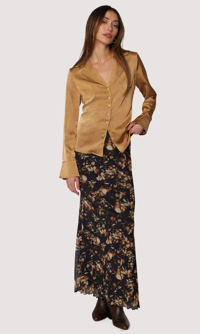 Woman wearing a gold jacket and floral skirt on a white background