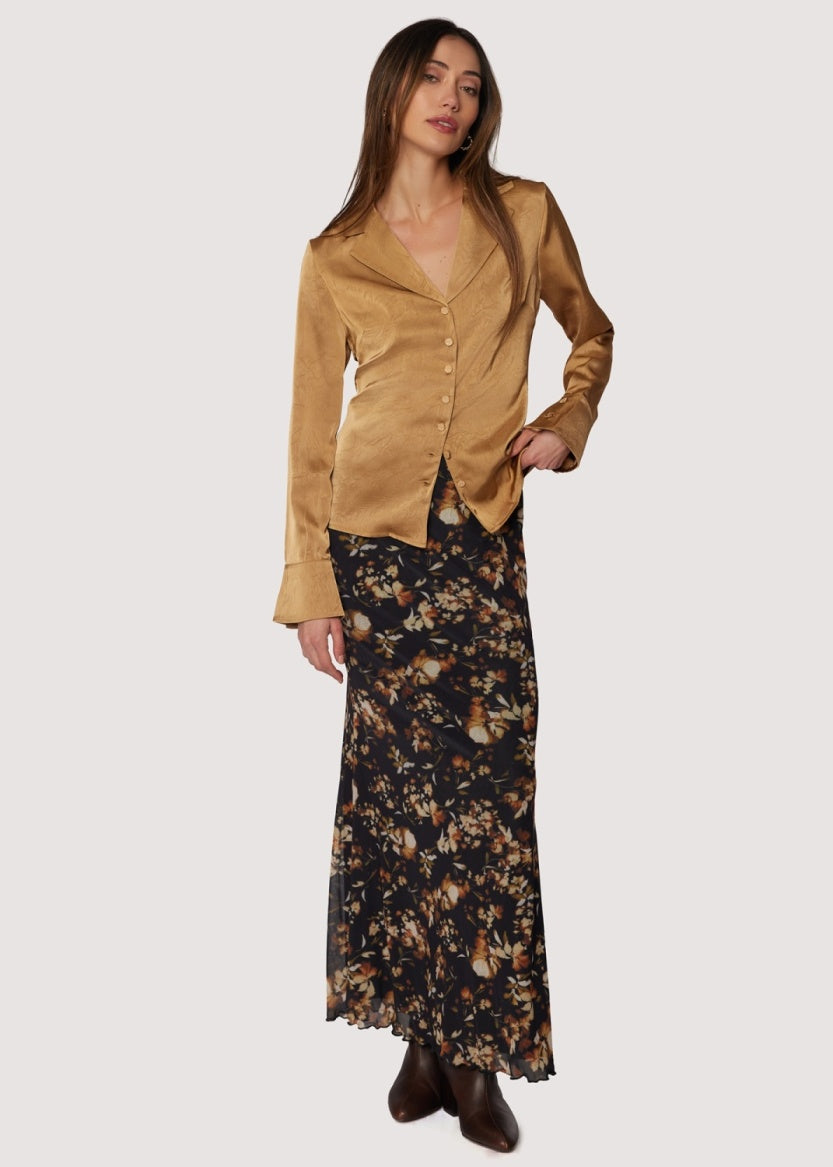 Woman wearing a gold jacket and floral skirt on a white background