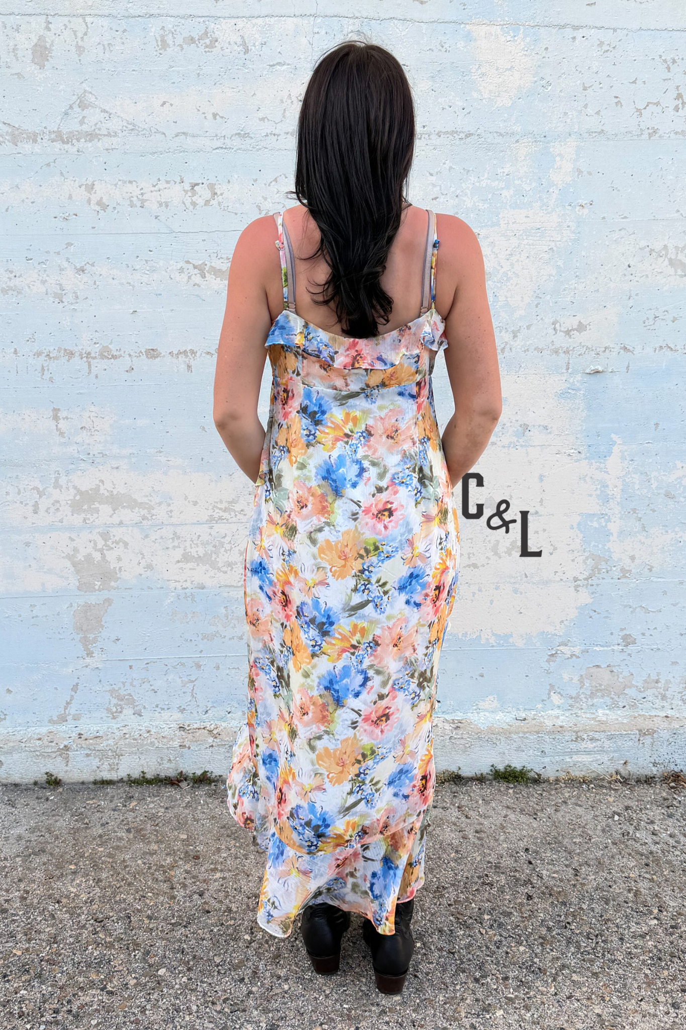 Woman wearing a floral dress standing in front of a textured wall with 'C&L' branding.