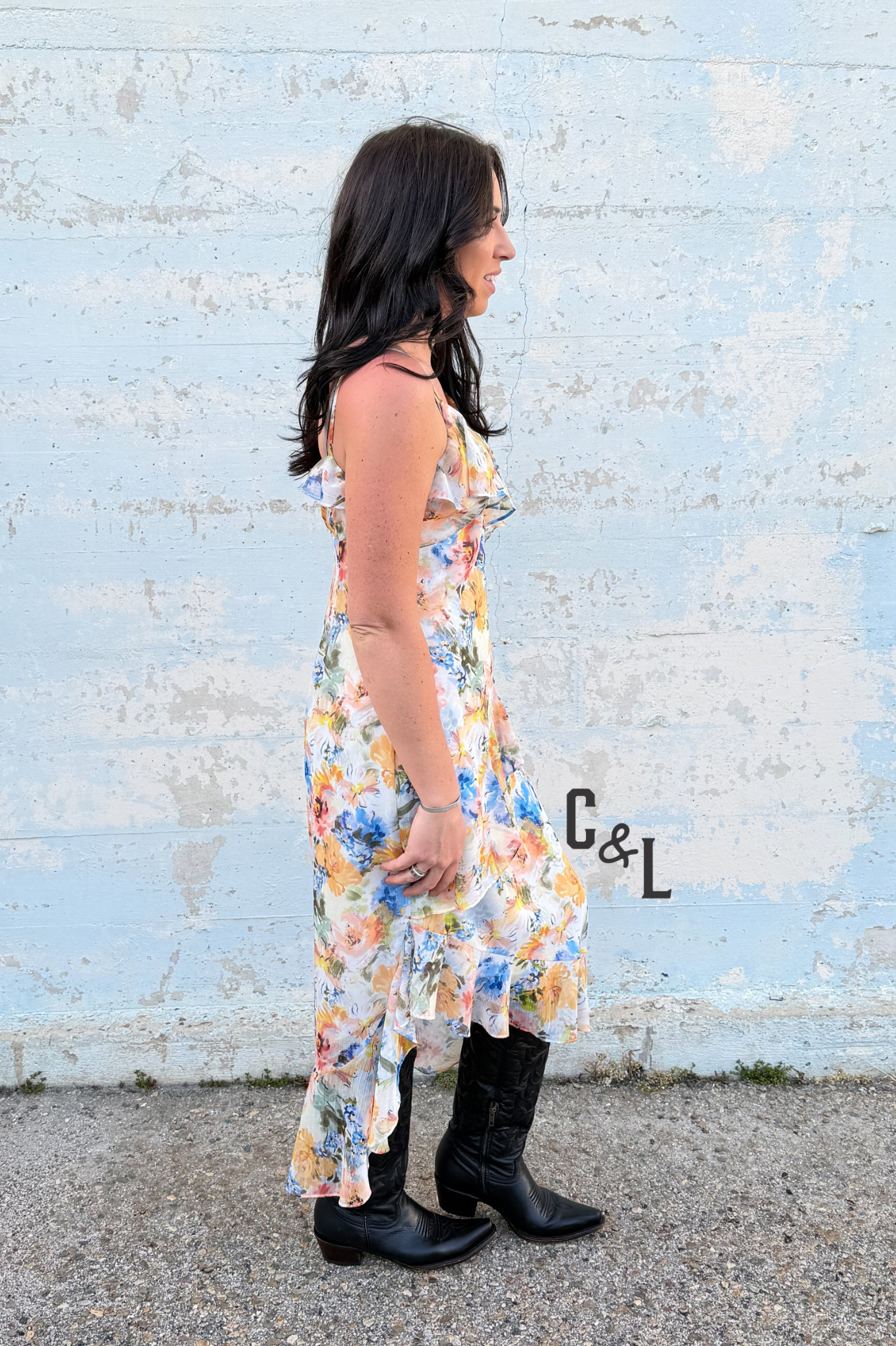 Woman in a floral dress and black boots standing against a textured blue wall.