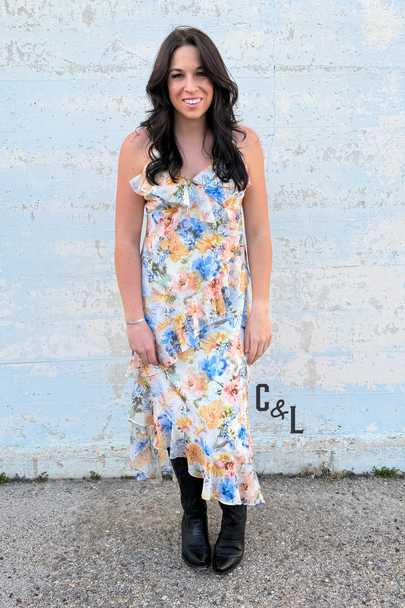 Woman wearing a floral dress standing against a textured wall with 'C&L' branding.