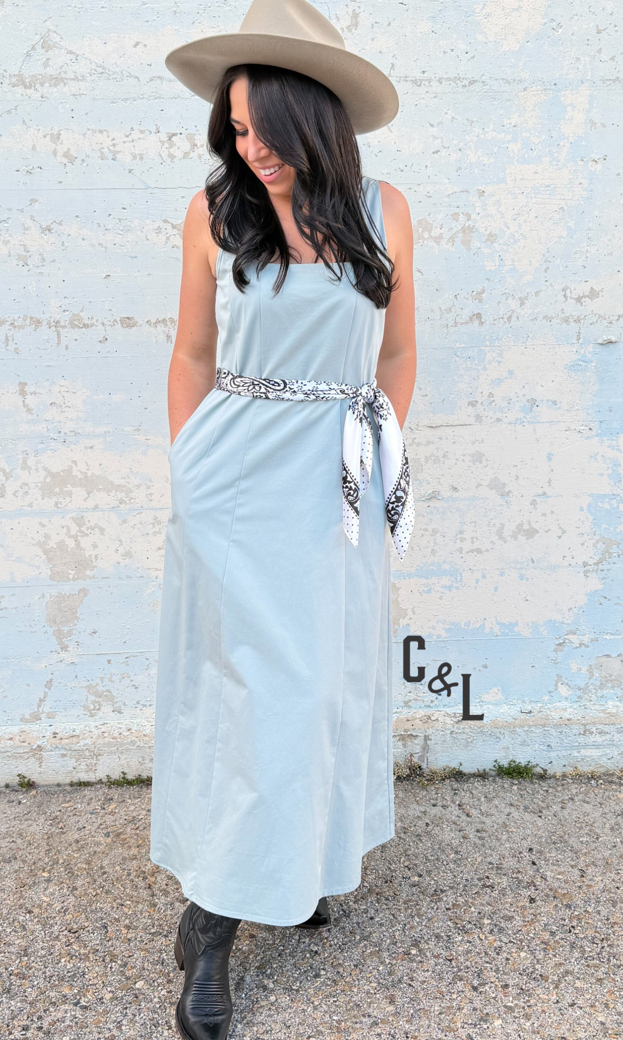 Woman wearing a light blue dress with a belt and a hat, standing against a textured wall.