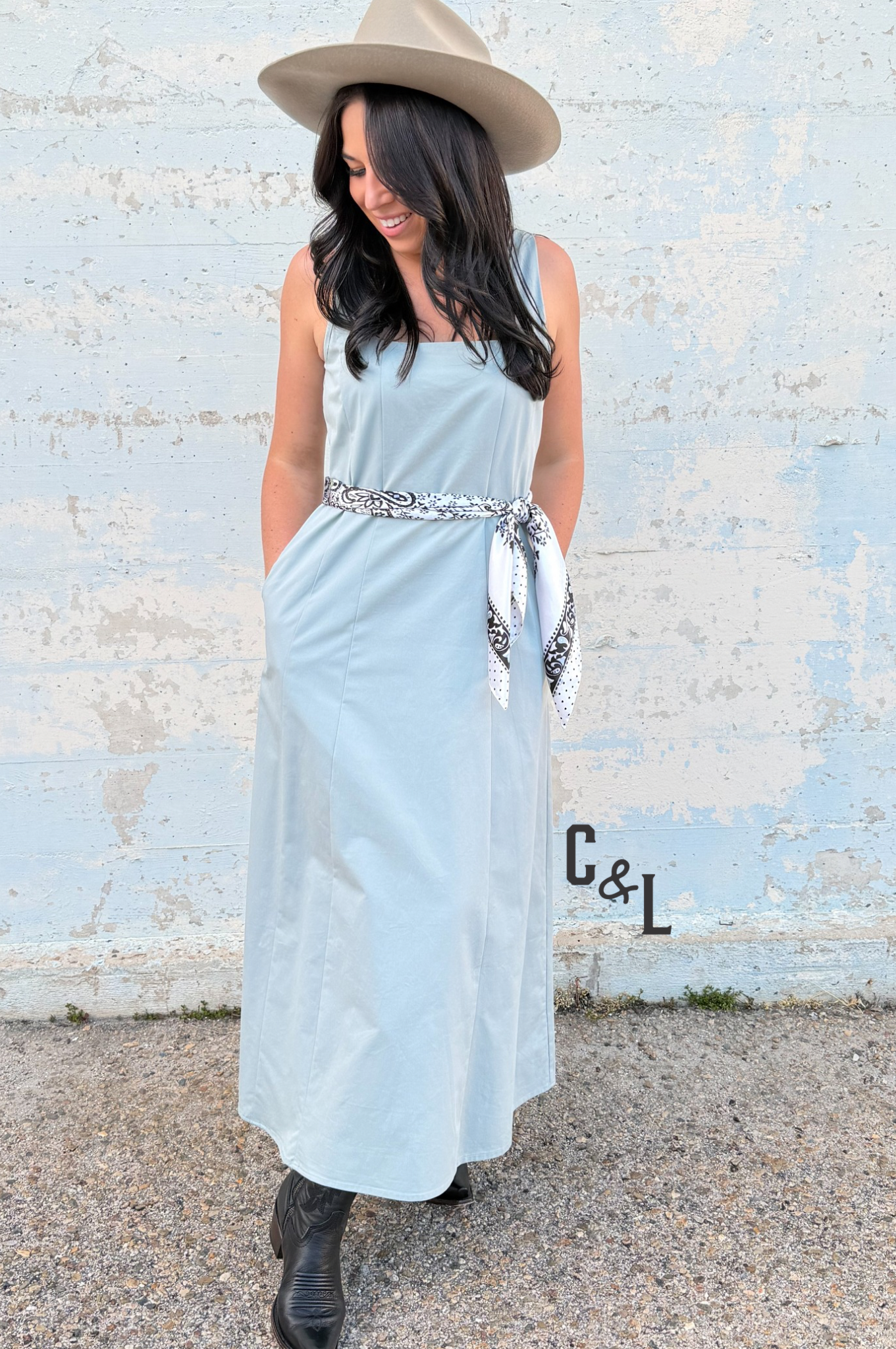 Woman wearing a light blue dress with a belt and a hat, standing against a textured wall.