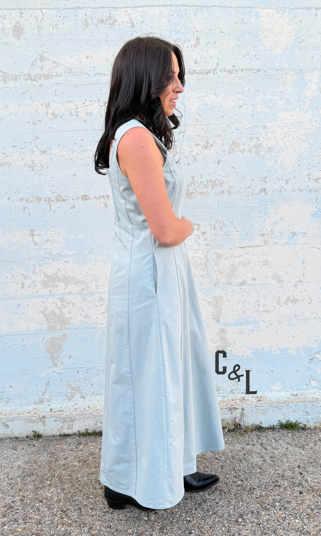 Woman in a light blue dress standing against a textured white wall.