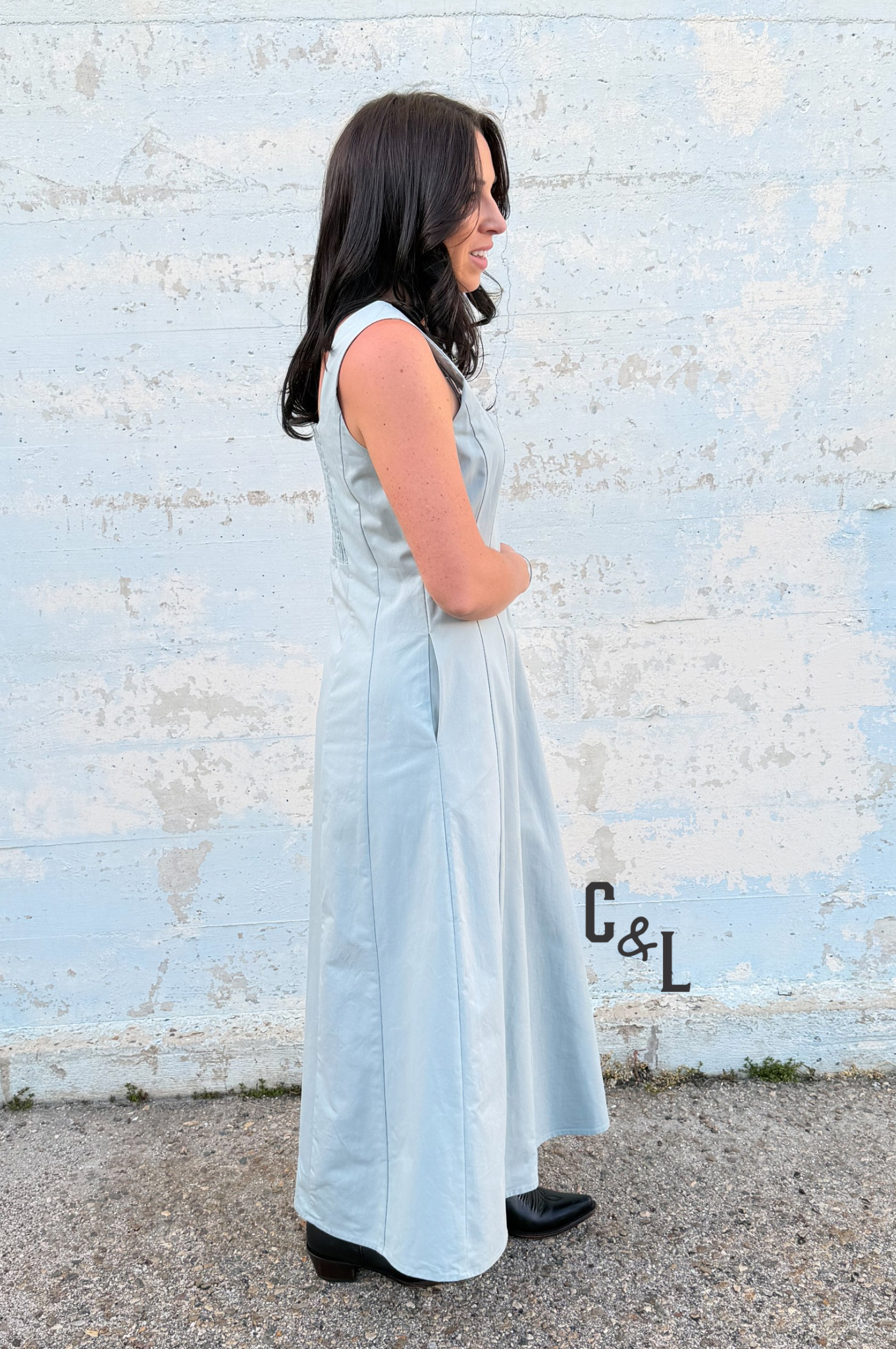 Woman in a light blue dress standing against a textured white wall.