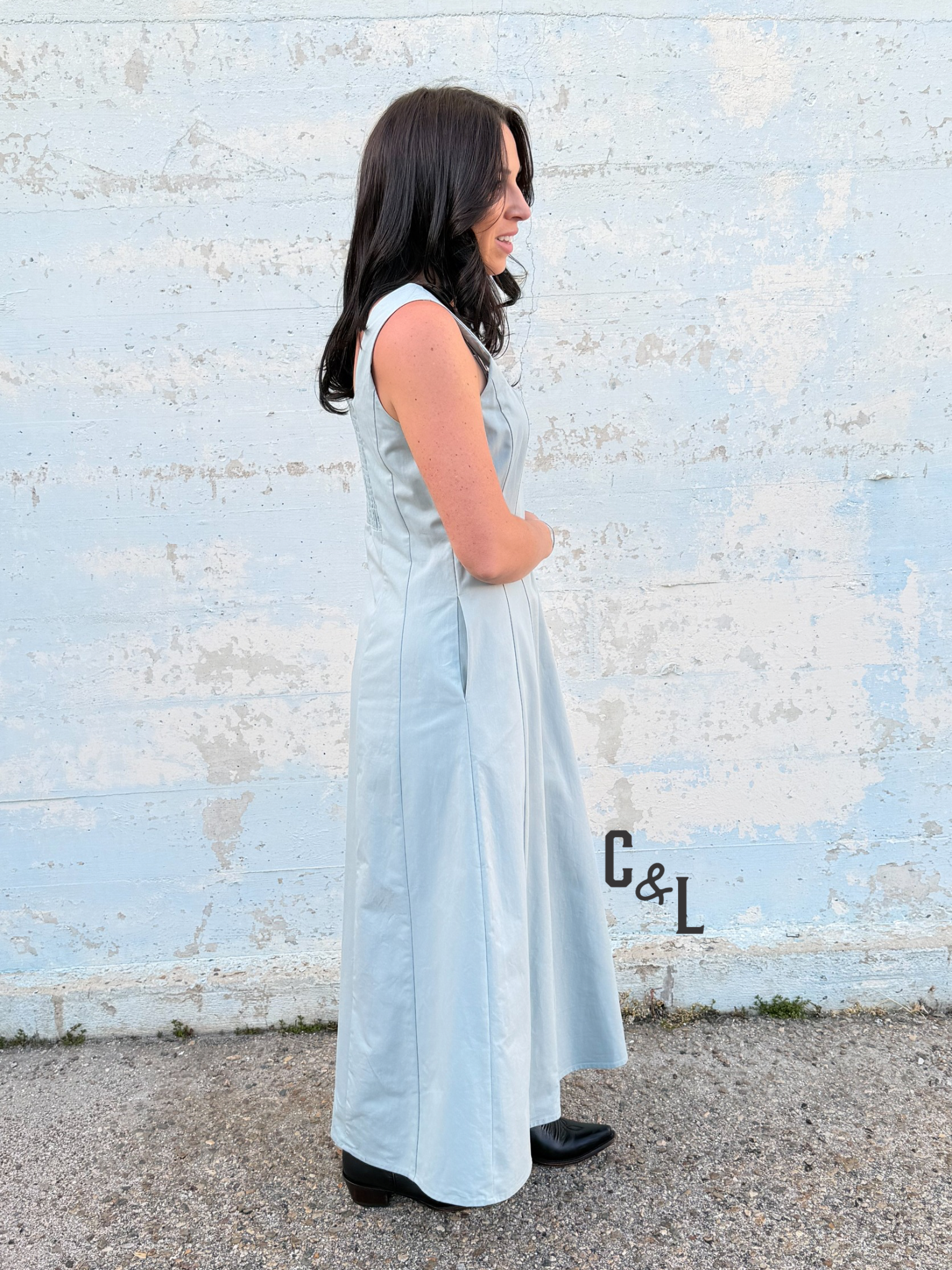 Woman in a light blue dress standing against a textured white wall.