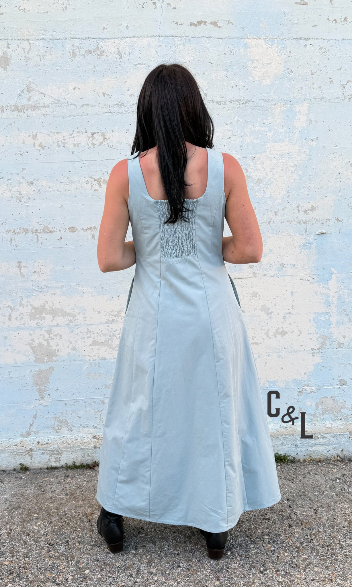 Woman wearing a light blue dress standing against a textured white wall.