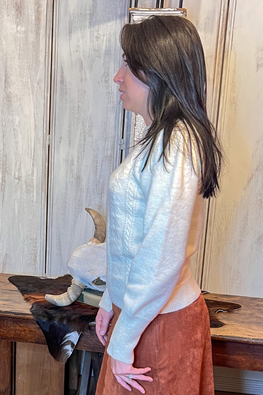 Woman wearing a ivory sweater standing in a room with wooden furniture and a fur rug.