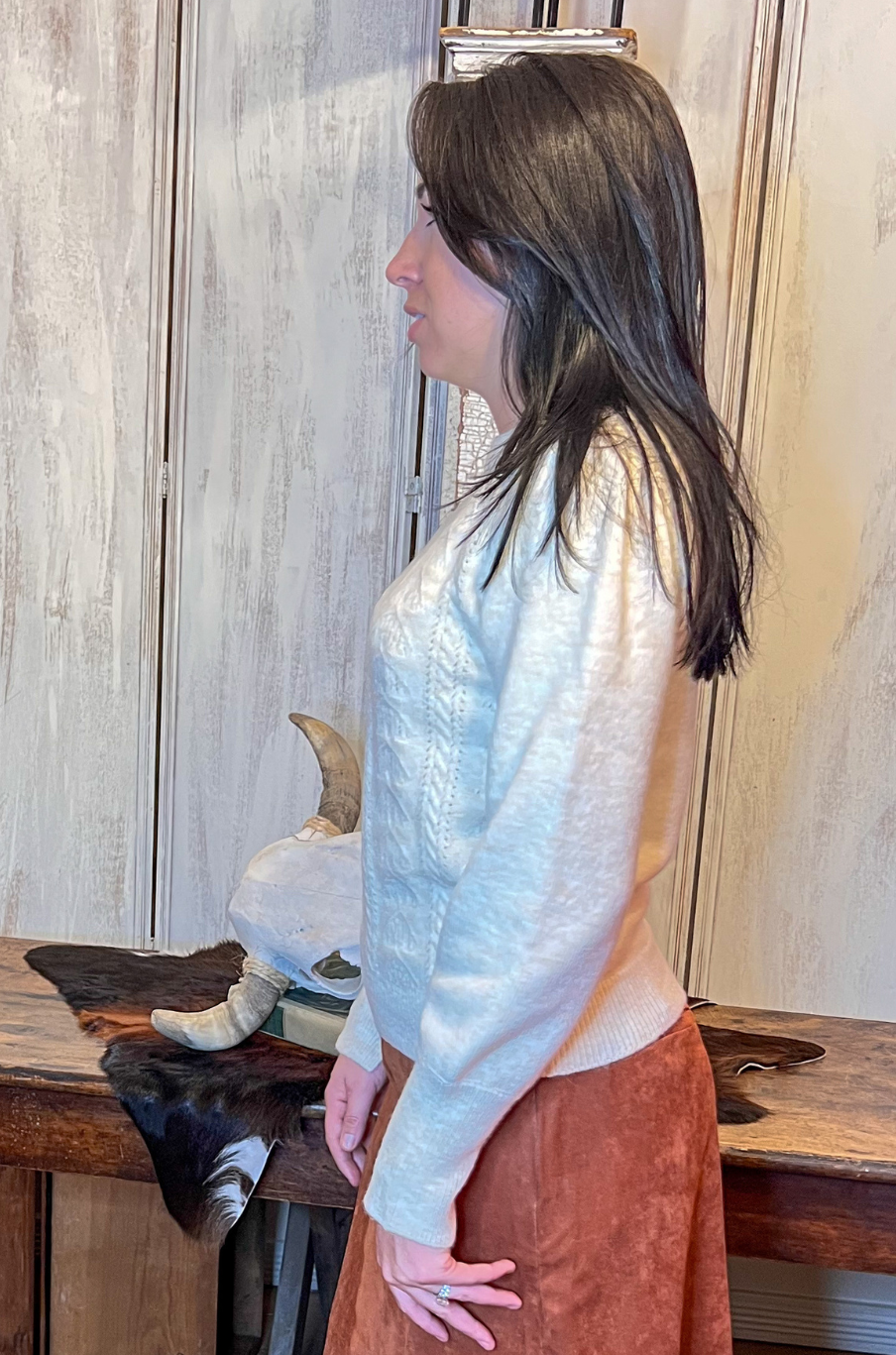 Woman wearing a ivory sweater standing in a room with wooden furniture and a fur rug.