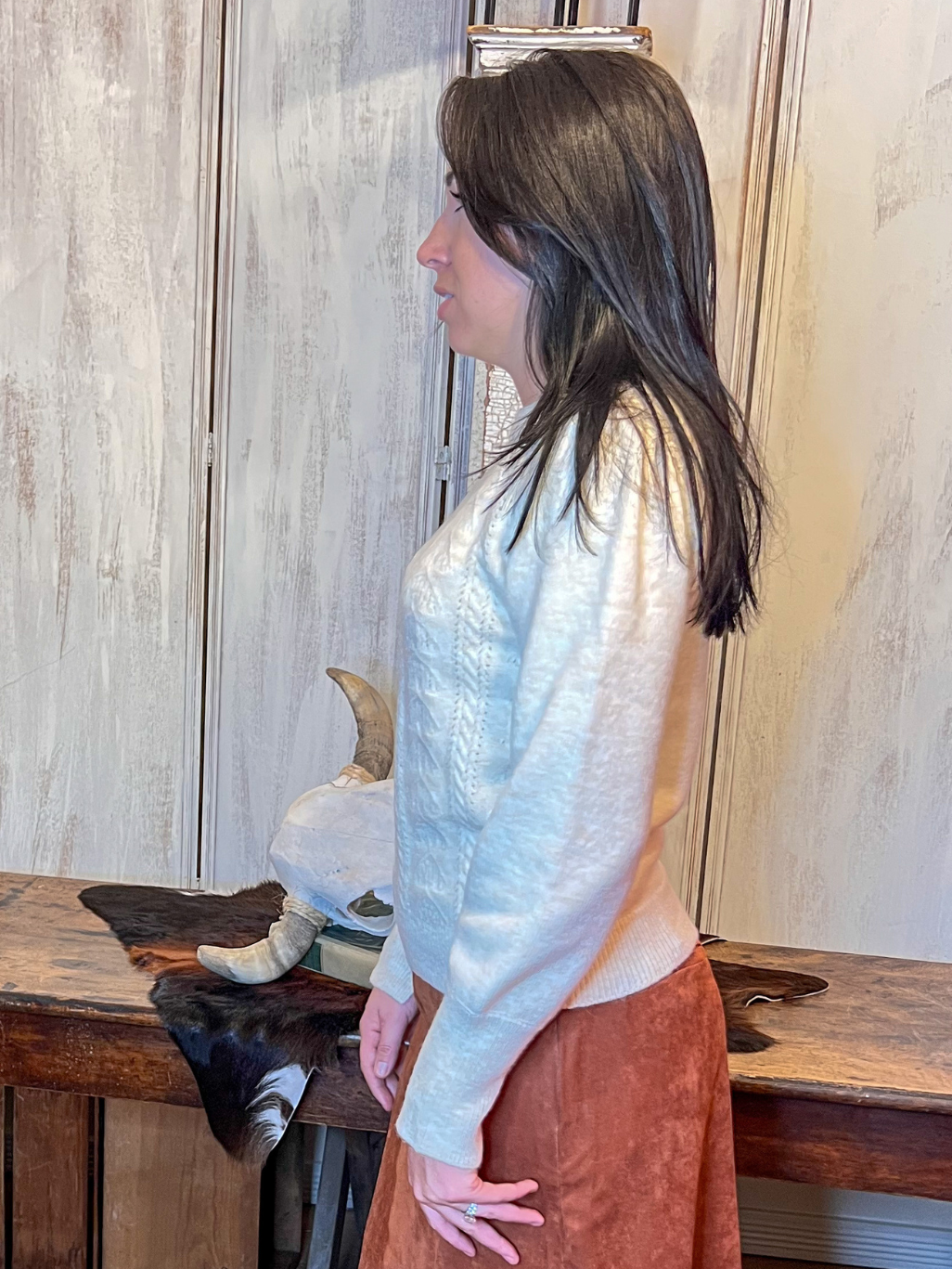 Woman wearing a ivory sweater standing in a room with wooden furniture and a fur rug.