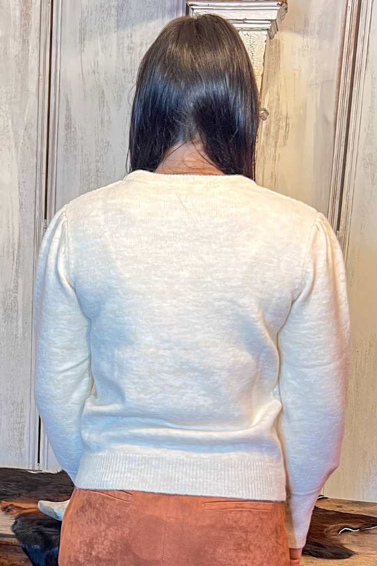 Person wearing a light-colored sweater and brown skirt standing in front of a wooden table.