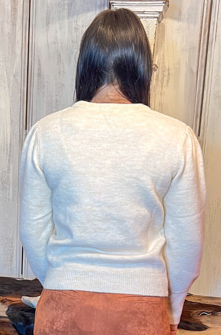 Person wearing a light-colored sweater and brown skirt standing in front of a wooden table.