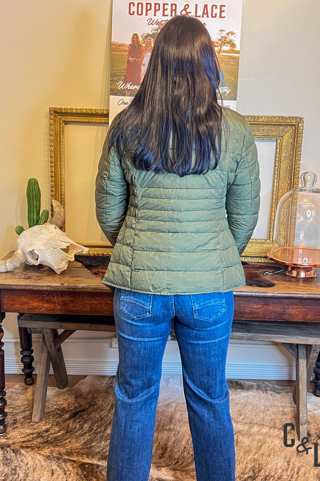 Person wearing a green puffer jacket and blue jeans standing in front of a table with decorative items.