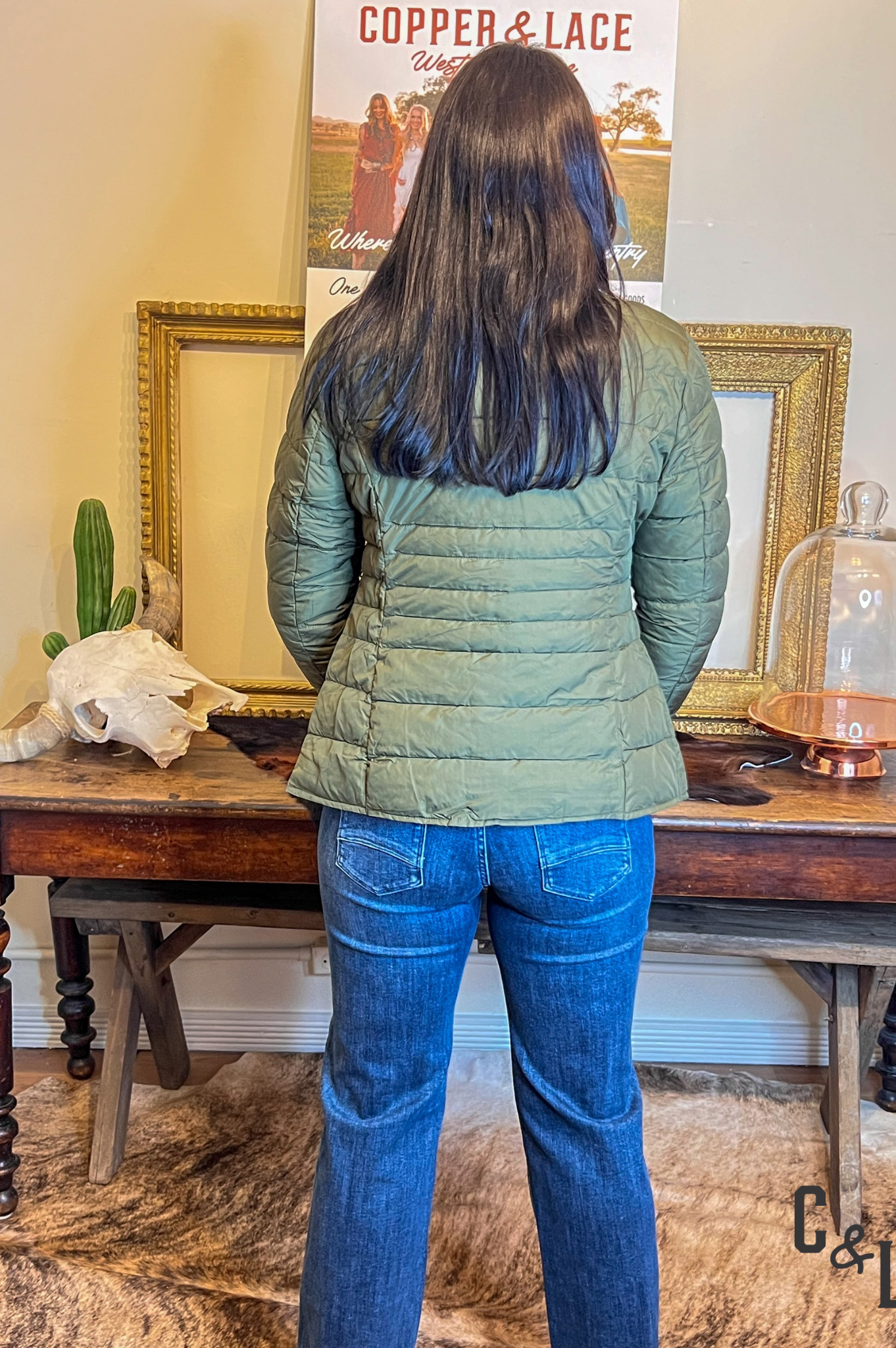 Person wearing a green puffer jacket and blue jeans standing in front of a table with decorative items.