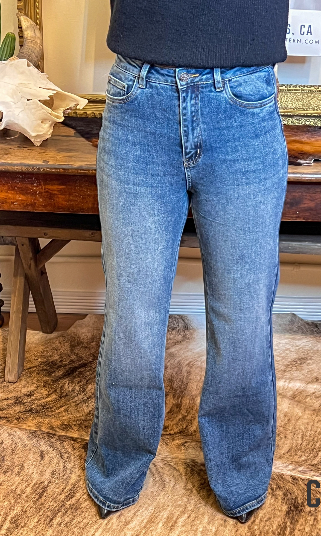 Person wearing blue jeans standing in a room with wooden furniture and decor.