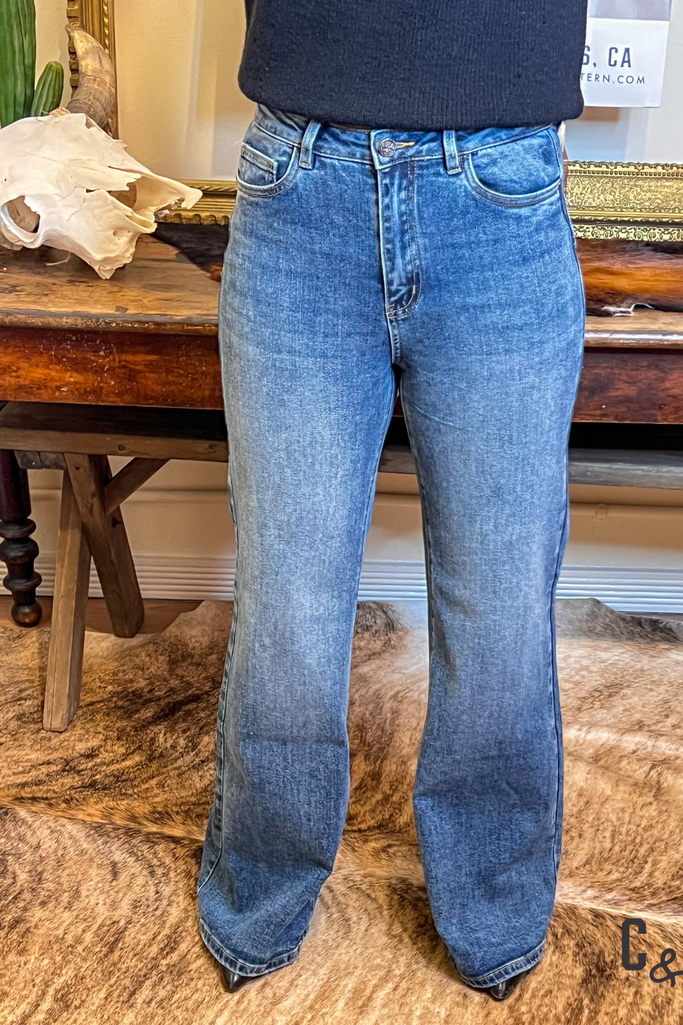 Person wearing blue jeans standing in a room with wooden furniture and decor.