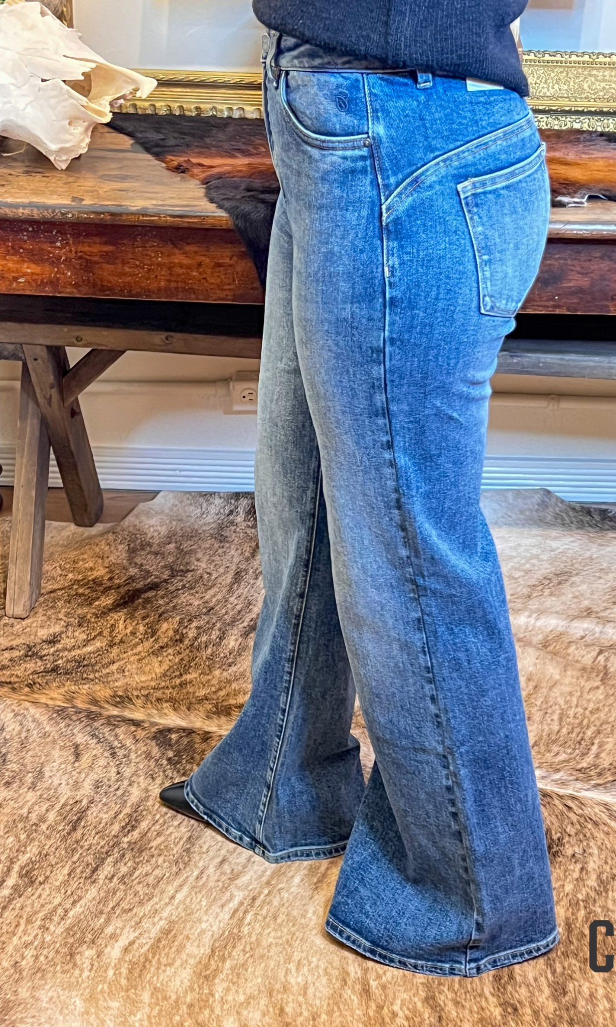 Person wearing blue jeans standing on a wooden floor with a rustic background