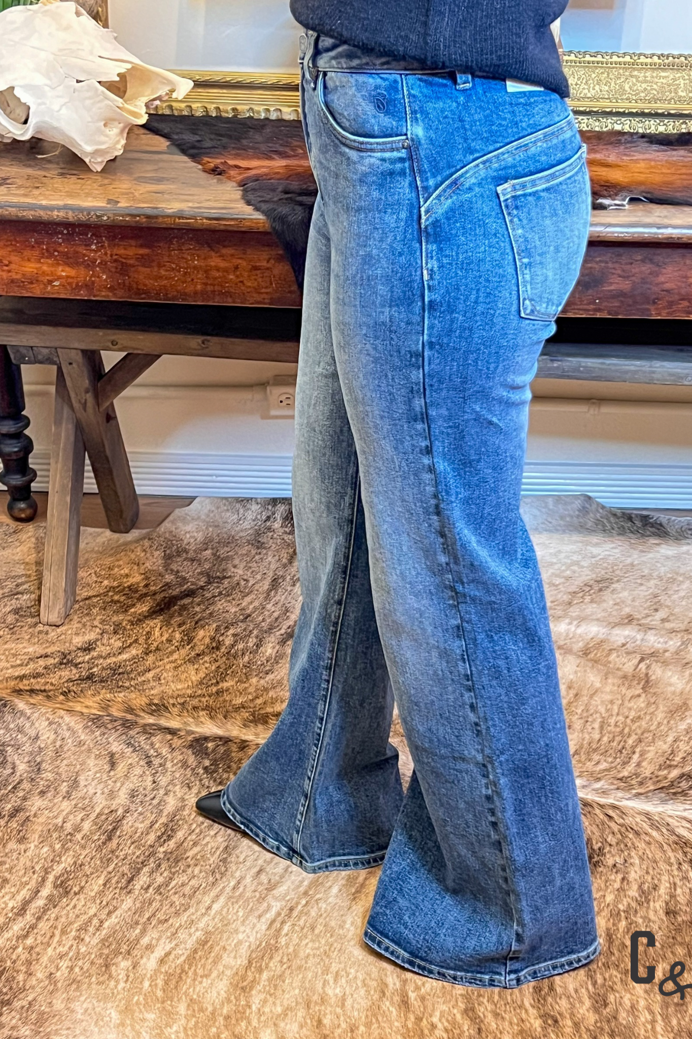 Person wearing blue jeans standing on a wooden floor with a rustic background