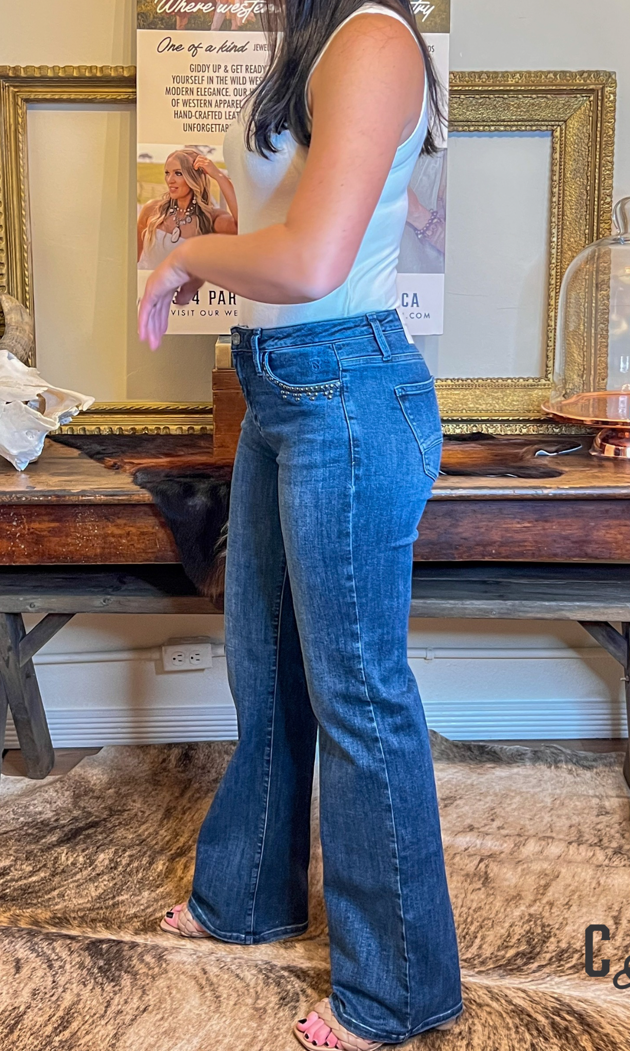 Person wearing blue jeans standing in a room with a wooden table and decorative items.