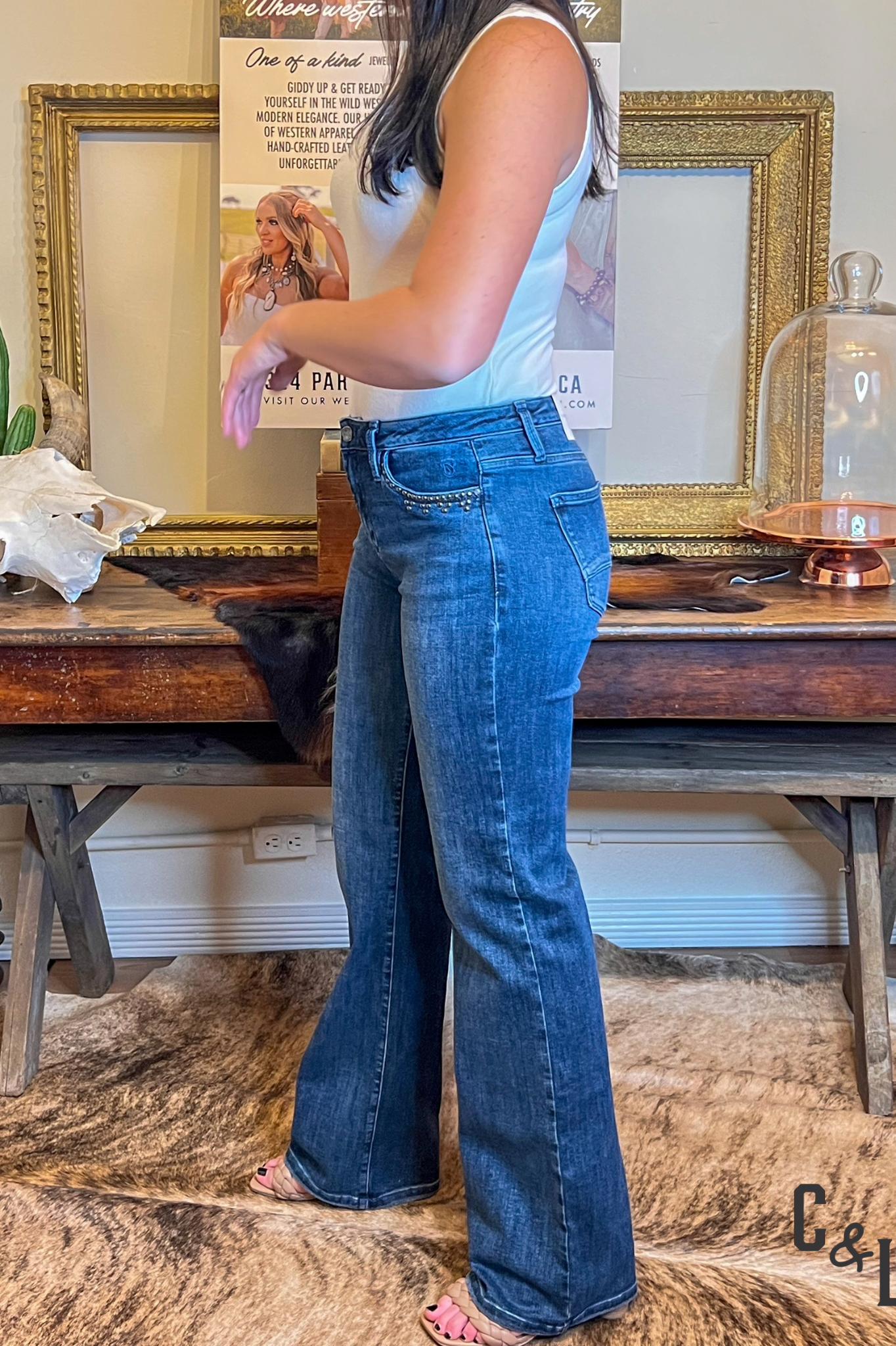 Person wearing blue jeans standing in a room with a wooden table and decorative items.