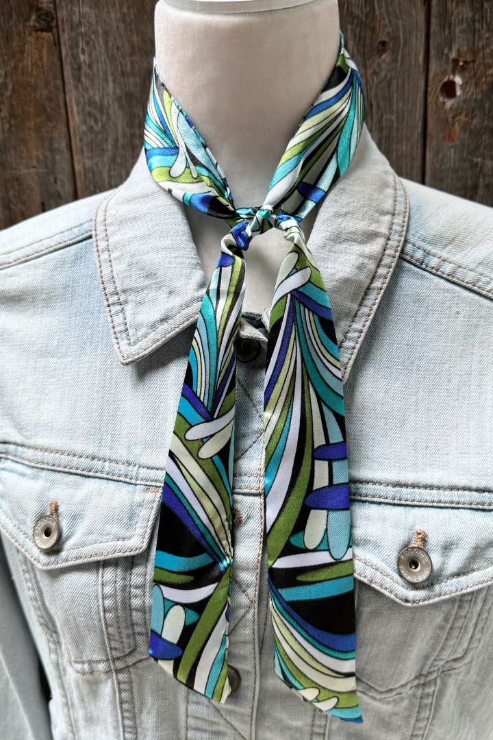 Mannequin wearing a light blue denim jacket with a colorful patterned scarf around its neck against a wooden background.